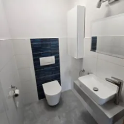 Nowoczesna łazienka po remoncie: biało-szare płytki, umywalka nablatowa na betonowym blacie, podwieszana toaleta i akcent z granatowych płytek.