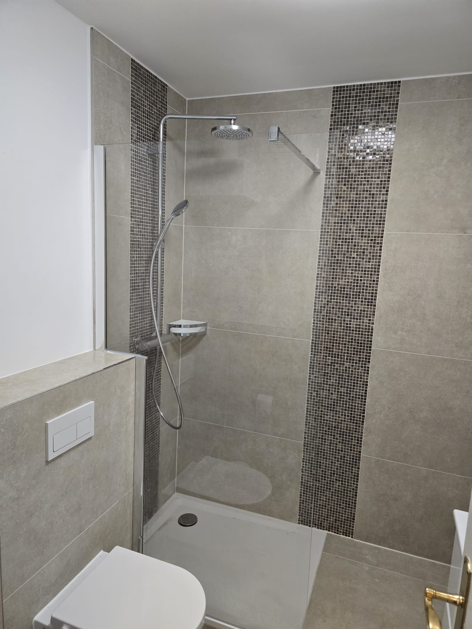 Nowoczesna łazienka po remoncie: kabina prysznicowa z mozaiką, beżowe płytki, podwieszana toaleta z przyciskiem. Minimalistyczny design, czyste linie.