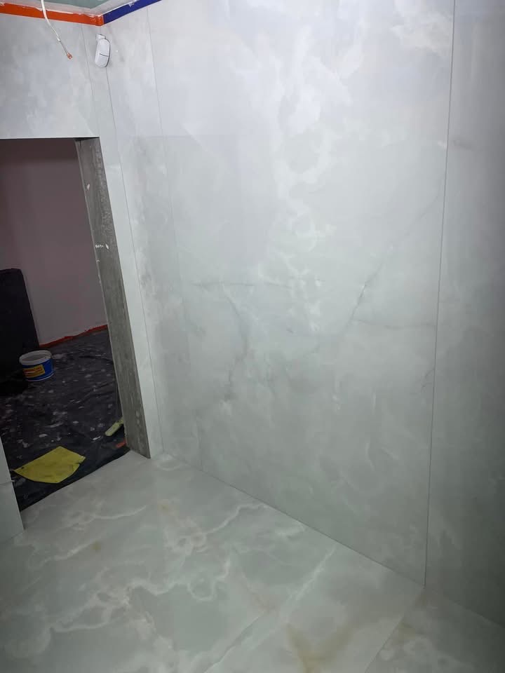 Wykończona łazienka z marmurowymi płytkami na ścianach i podłodze. Widoczne detale wykończeniowe i fragment wnętrza przedpokoju z narzędziami.