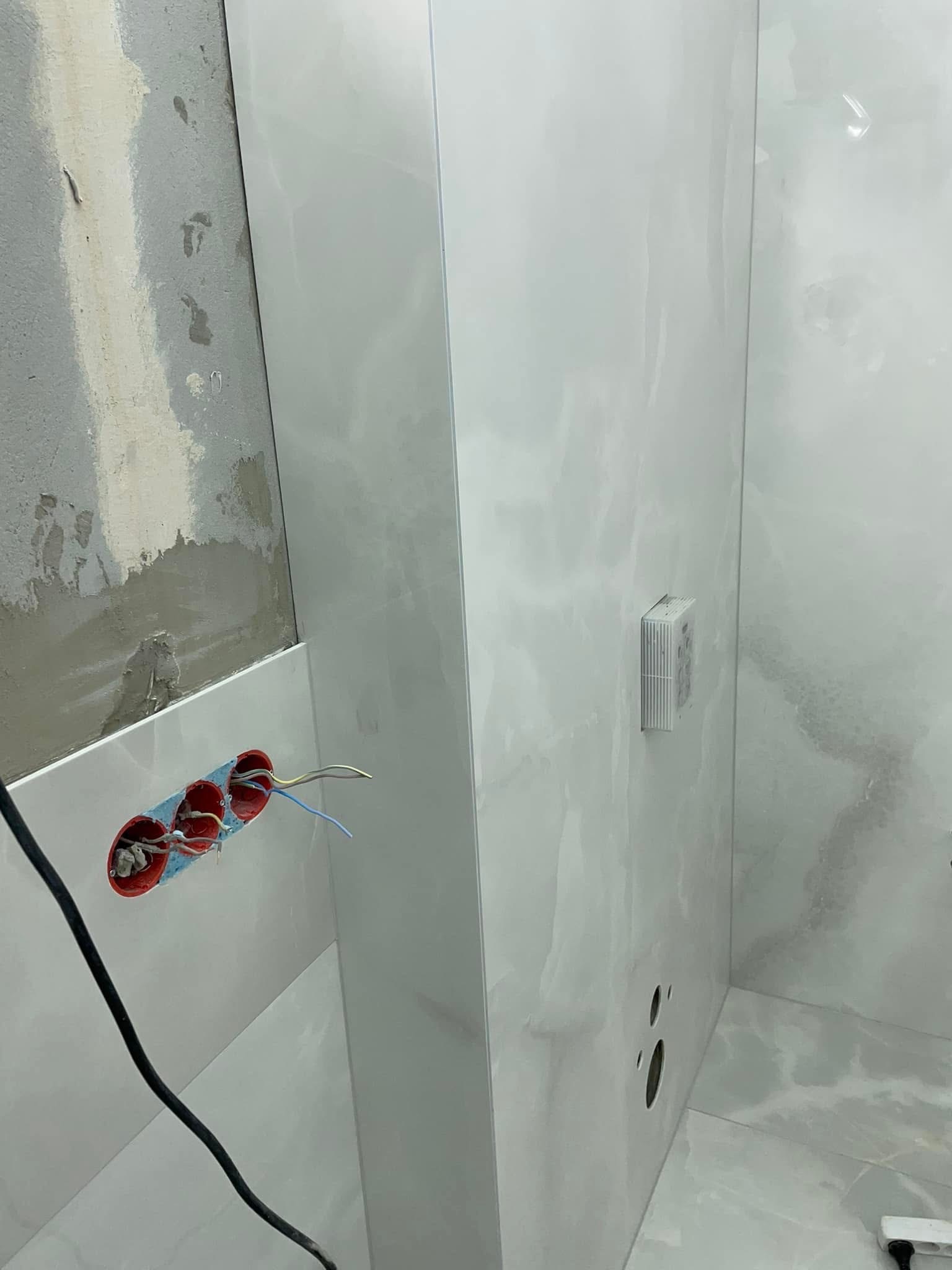 Łazienka w trakcie remontu: częściowo ułożone spieki kwarcowe, widoczne puszki elektryczne i fragment ściany przed wykończeniem. Prace glazurnicze w toku.