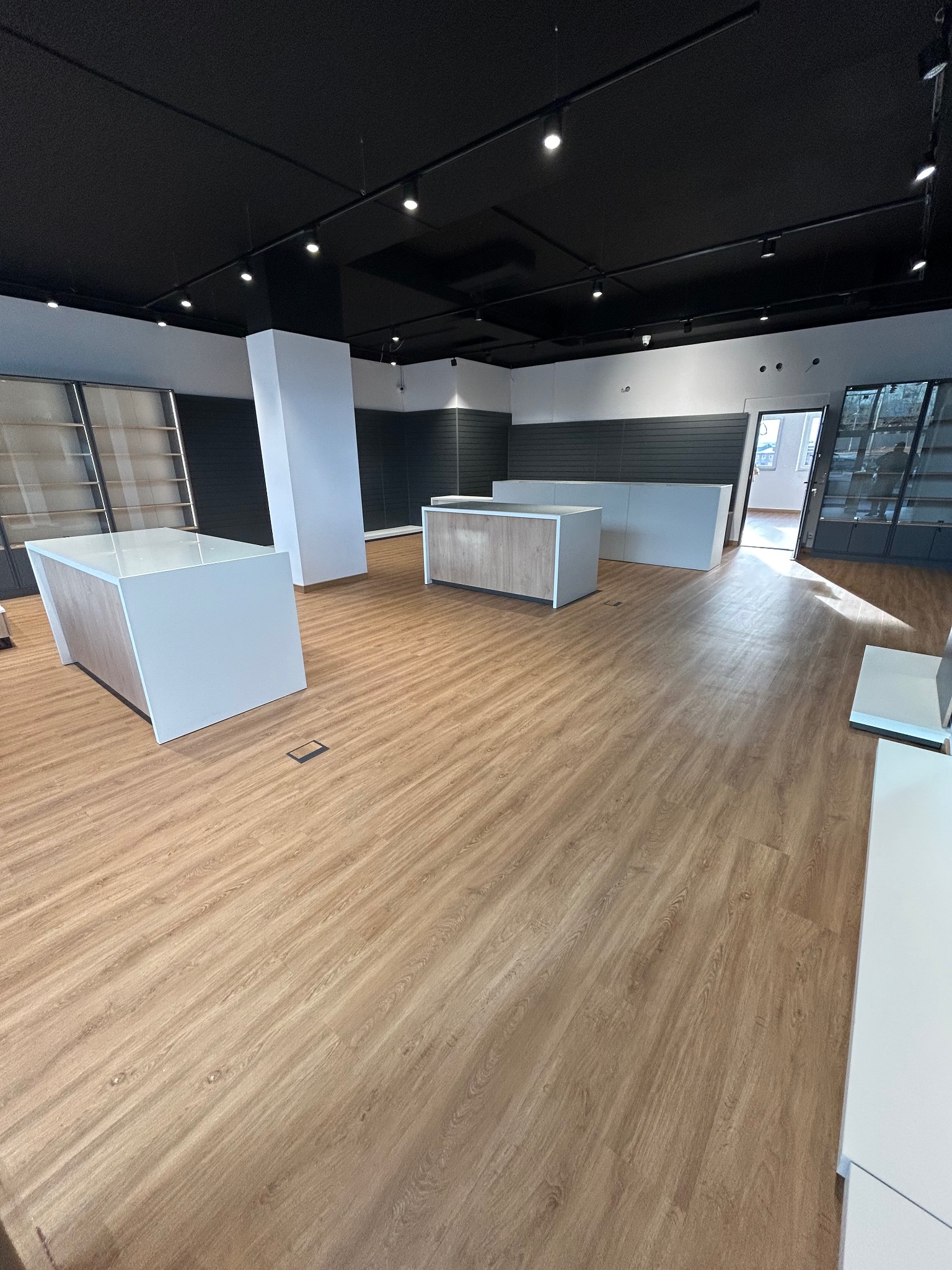 Wnętrze sklepu po remoncie: drewniana podłoga, białe lady i czarny sufit z oświetleniem punktowym. Widoczne regały i pionowe panele ścienne w kolorze szarym.