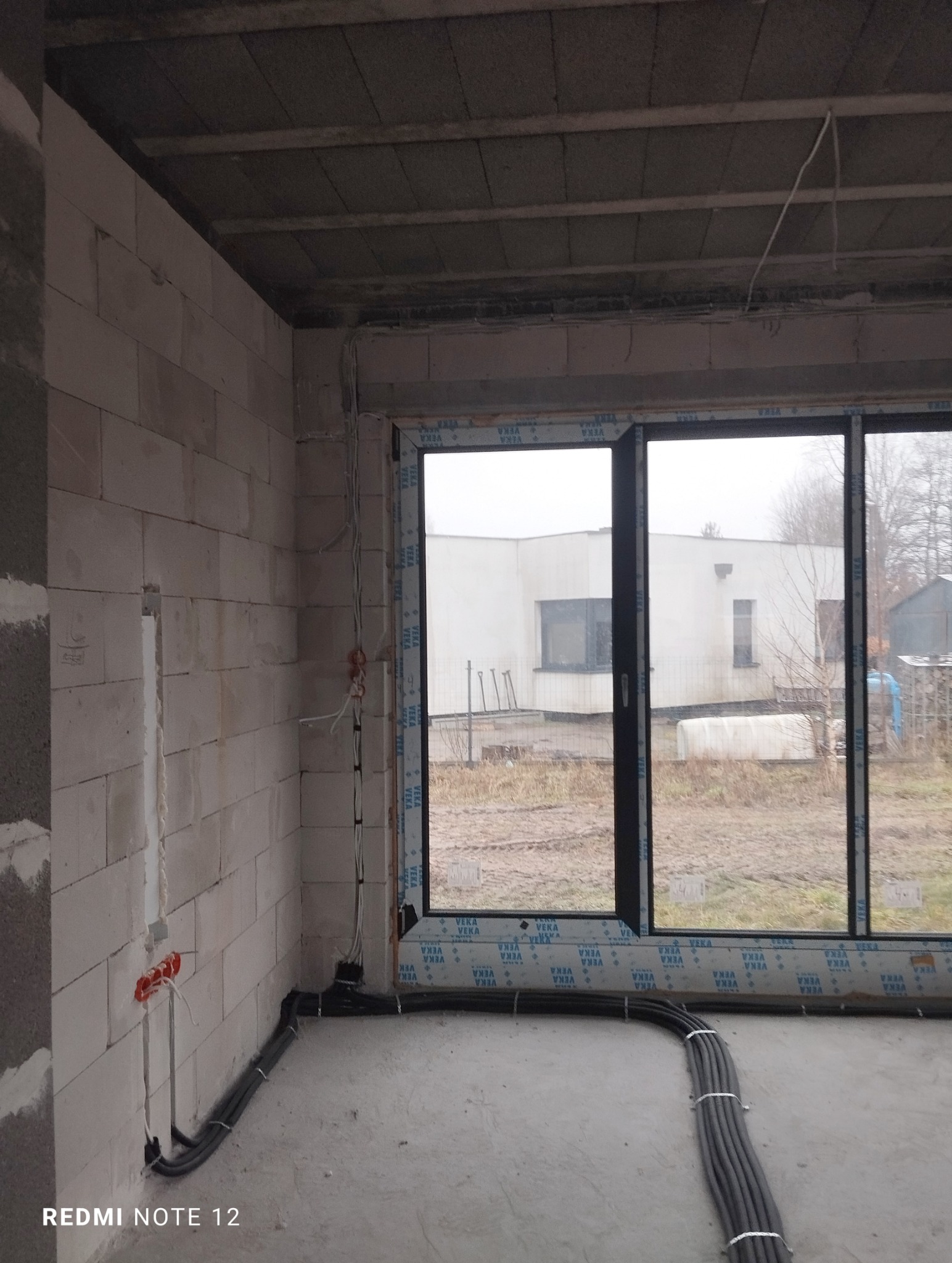 Surowy stan: instalacja elektryczna w nowym domu w Wilcze. Widoczne kable w peszlach prowadzone po podłodze i wyprowadzone gniazdka w ścianie z betonu komórkowego.