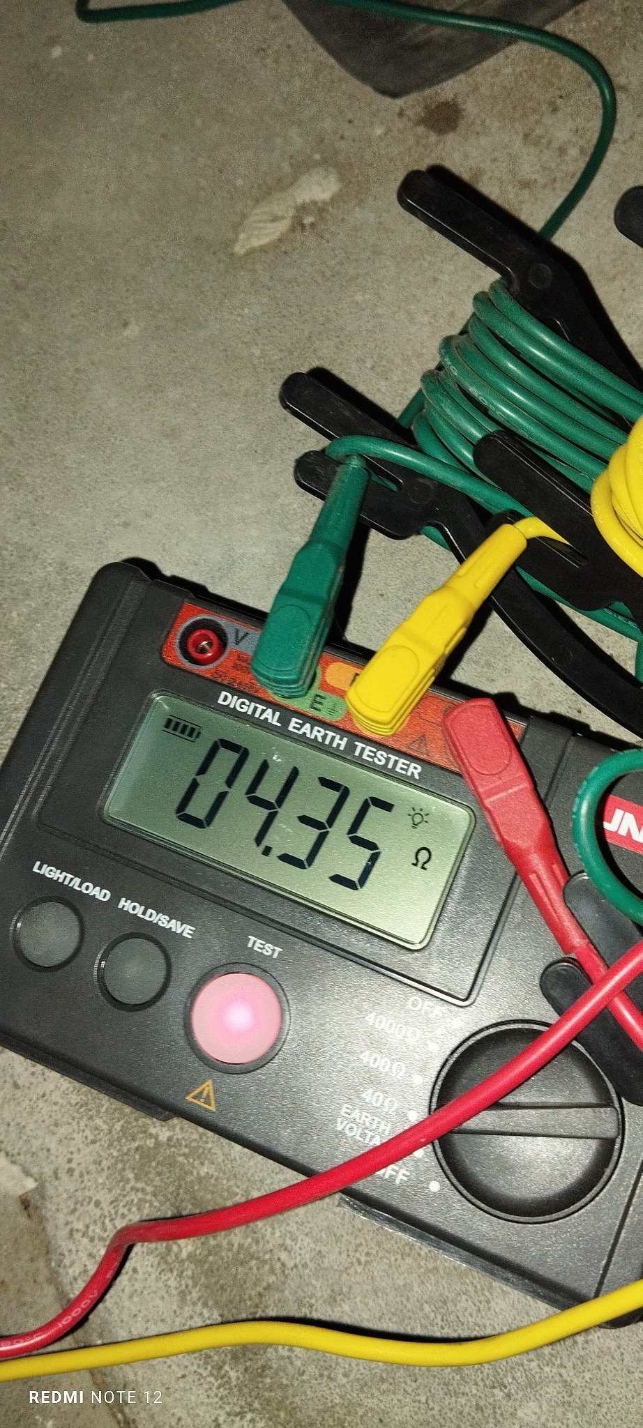 Miernik rezystancji uziomu wyświetla wynik 04.35 Ω, z widocznymi przewodami pomiarowymi w kolorach: czerwonym, żółtym i zielonym. Urządzenie leży na szarej powierzchni.