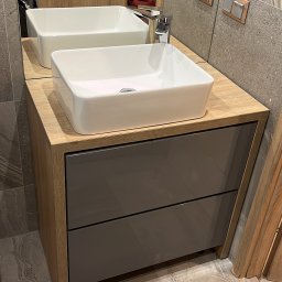 SZYMUR - Nowoczesna łazienka: biała, prostokątna umywalka nablatowa na szafce z szarymi frontami, drewnopodobny blat i płytki imitujące kamień na ścianie i podłodze.