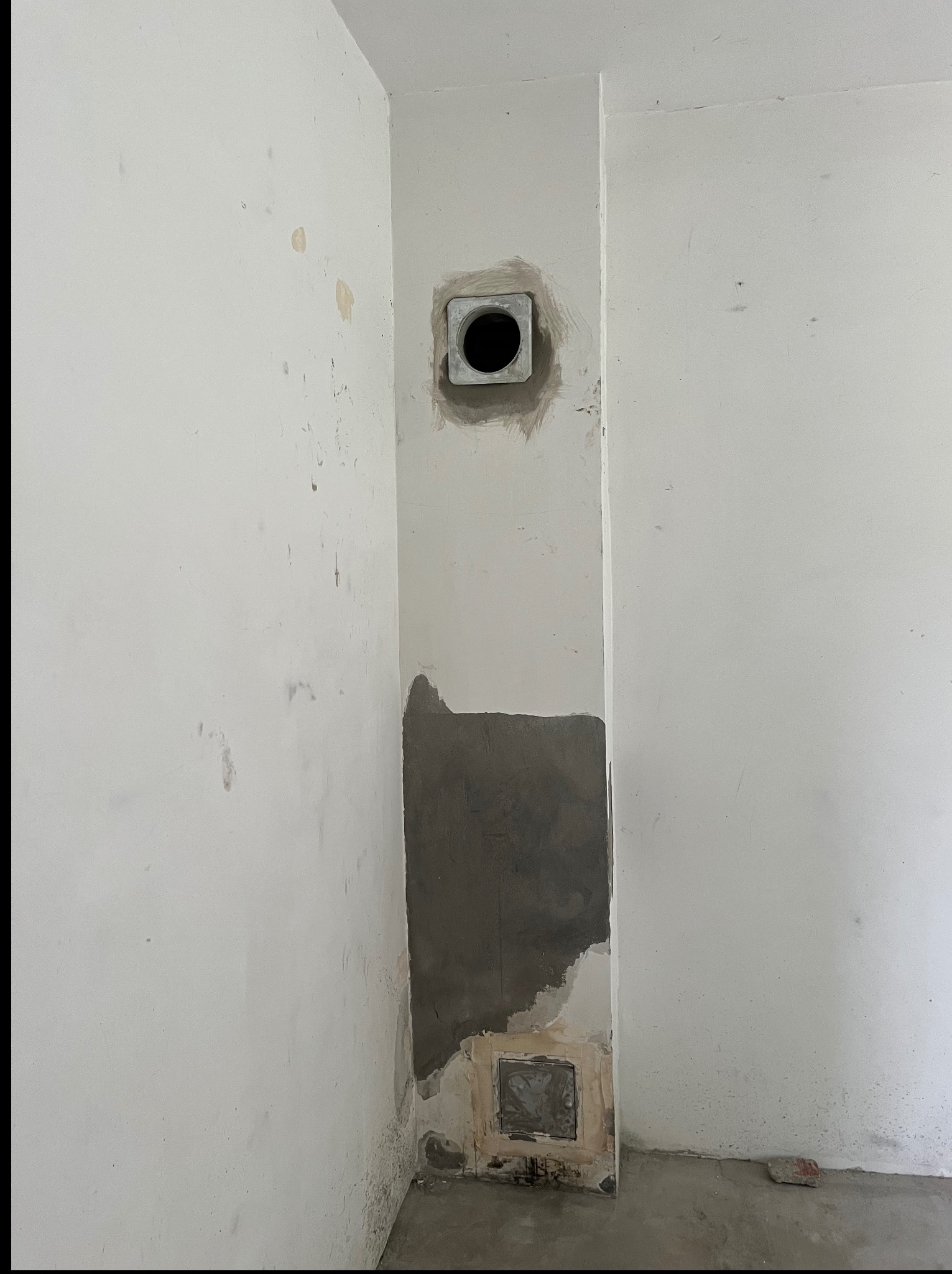 Fragment ściany w trakcie prac przygotowawczych: szpachlowanie ubytków i otworu wentylacyjnego. Widoczne ślady po wcześniejszych pracach i surowy beton na podłodze.