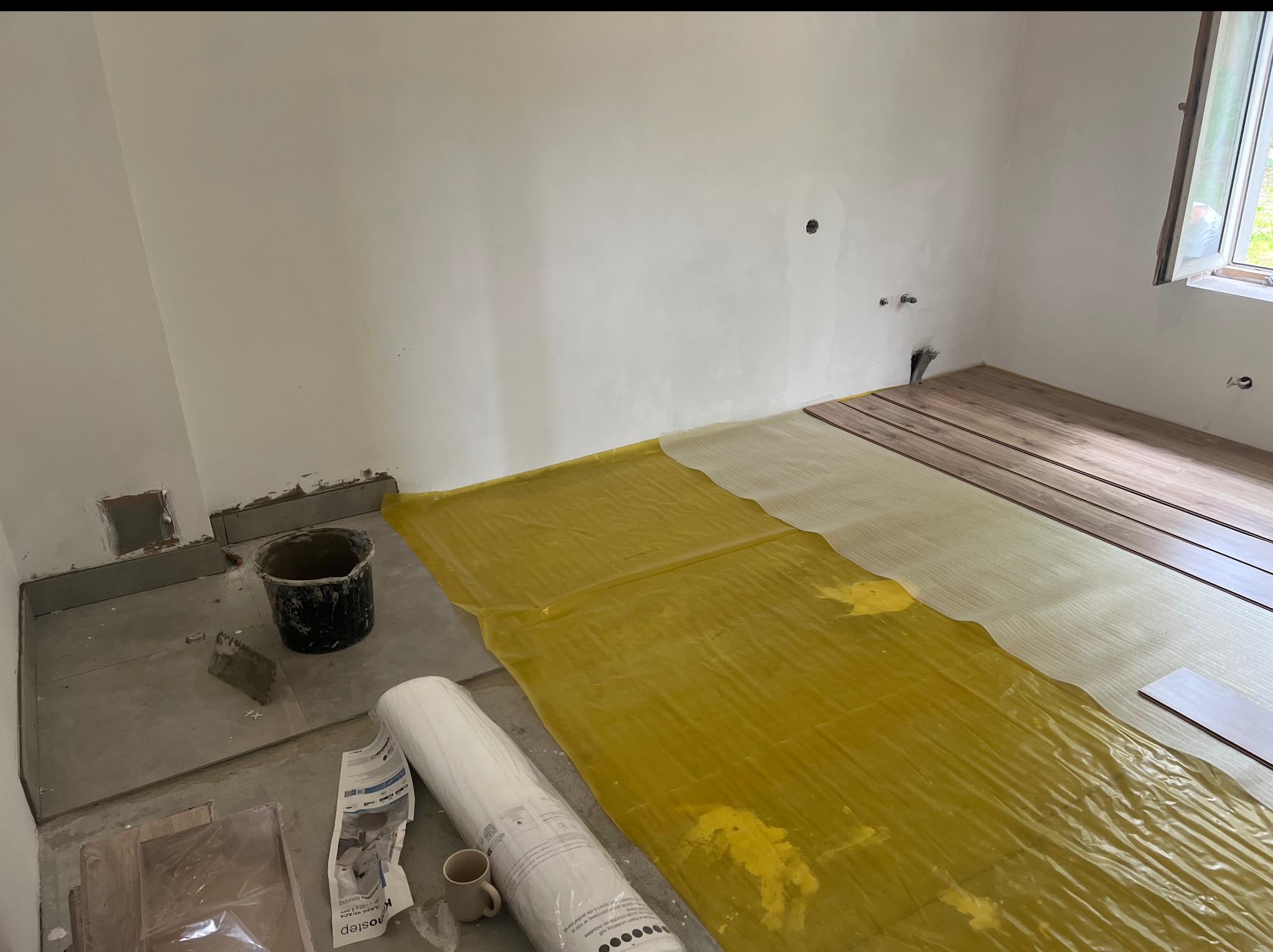 Układanie paneli podłogowych w pokoju: folia paroizolacyjna, podkład, panele. Widoczne narzędzia i materiały budowlane. Etap prac wykończeniowych.