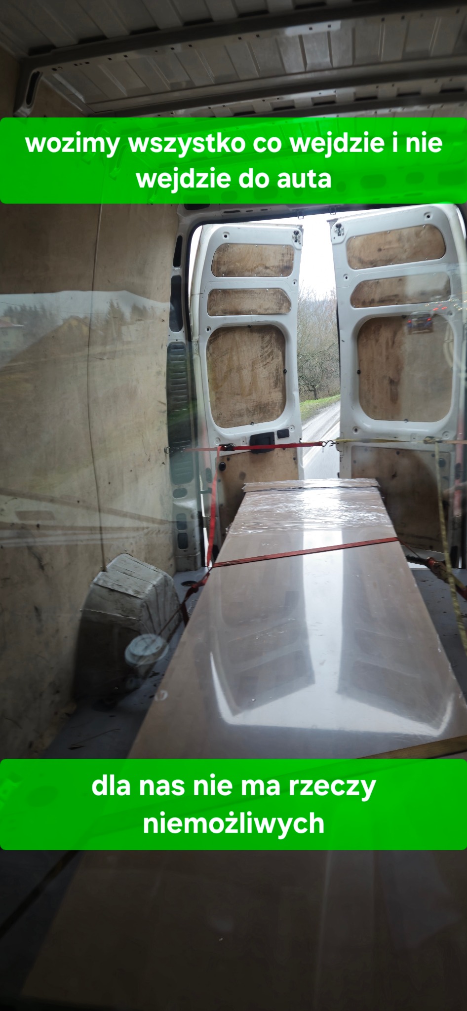 Wnętrze busa z otwartymi drzwiami, zabezpieczony ładunek w folii, widok na drogę. Tekst: 'wozimy wszystko co wejdzie i nie wejdzie do auta, dla nas nie ma rzeczy niemożliwych'.