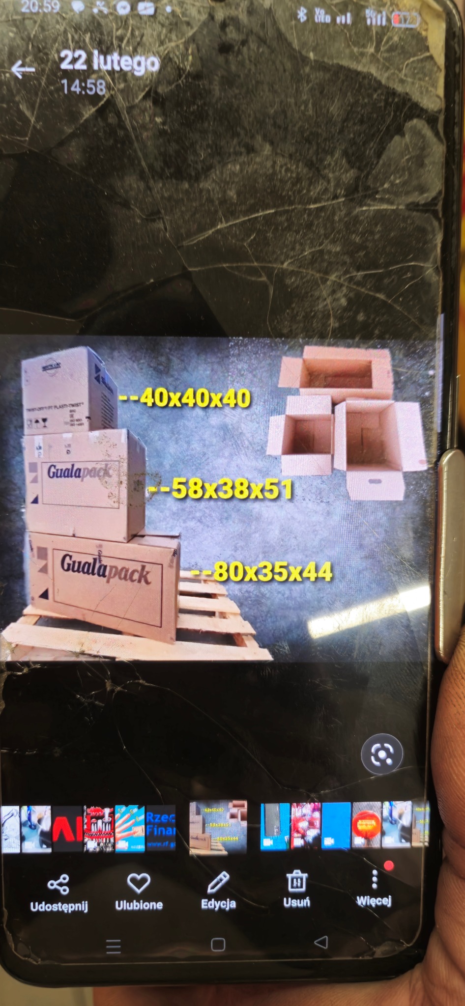 Zdjęcie ekranu telefonu z pękniętym szkłem, na którym widoczne są kartony do pakowania o wymiarach 40x40x40, 58x38x51 i 80x35x44, ułożone na palecie.