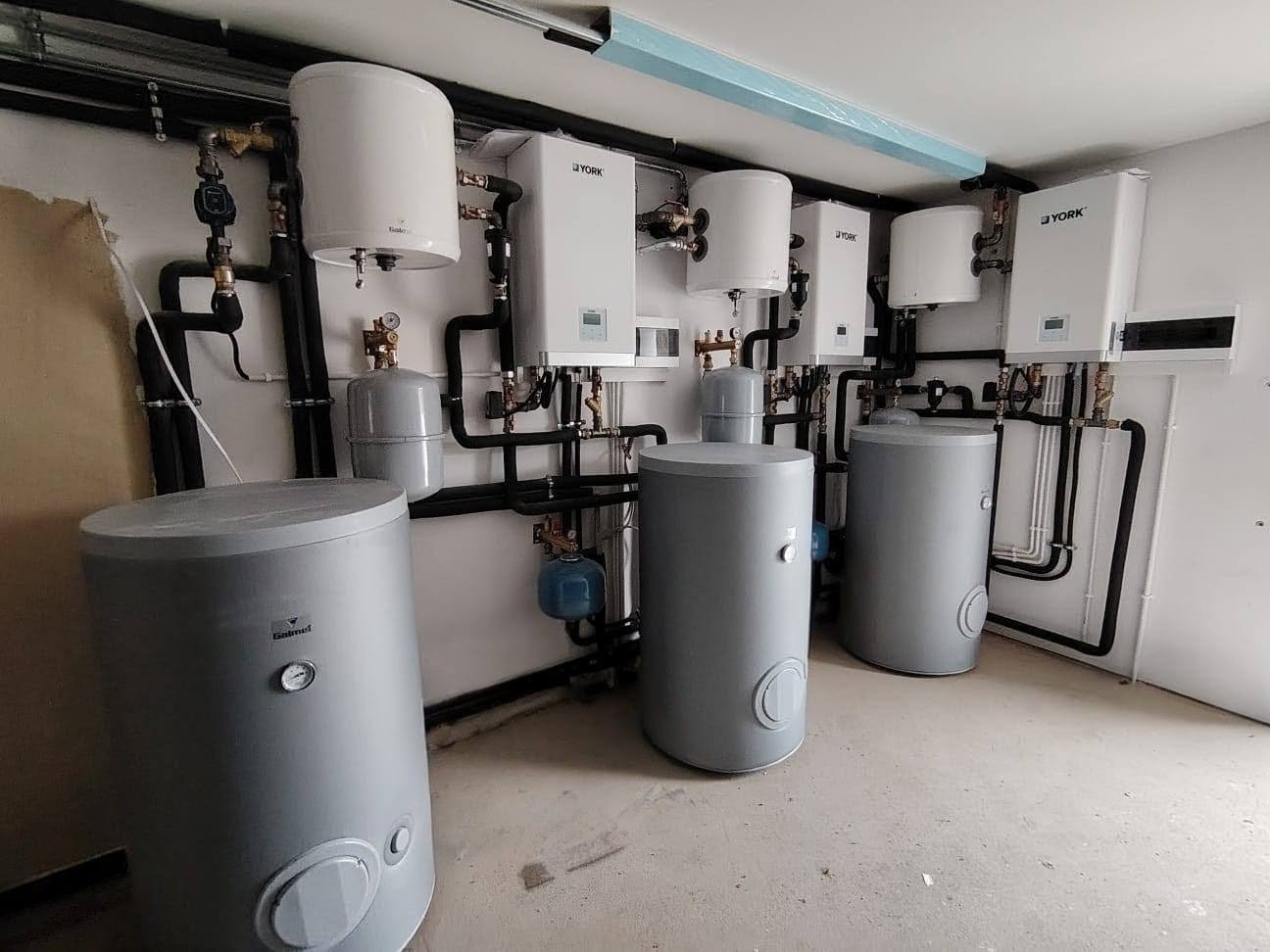 Kompletna instalacja grzewcza z kilkoma zbiornikami i urządzeniami York, z widocznymi rurami i elementami montażowymi w jasnym pomieszczeniu.