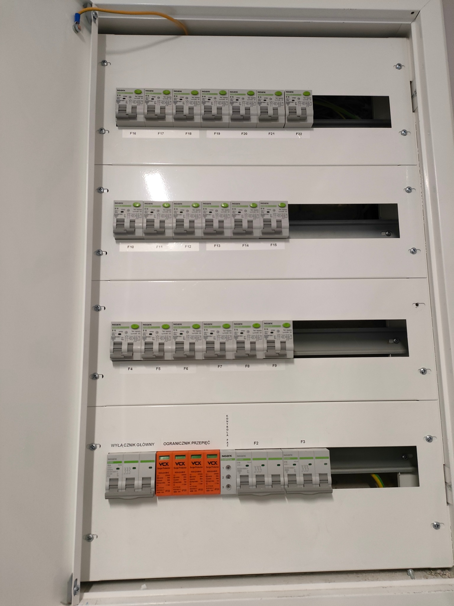 Rozdzielnica elektryczna z bezpiecznikami NOARK i ogranicznikami przepięć VCX w białej obudowie, widoczne przewody.