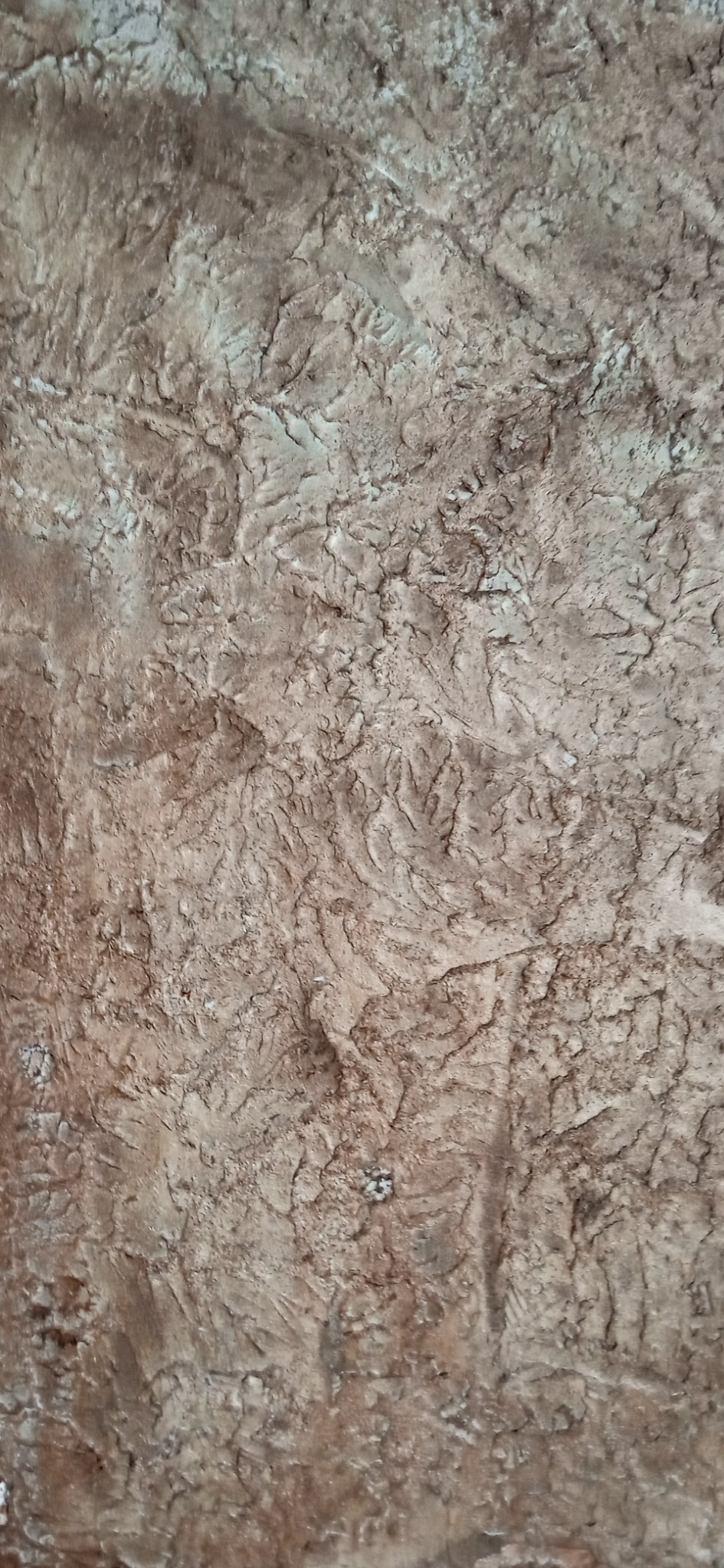 Dekoracyjna struktura ściany w odcieniach beżu i brązu, imitująca naturalny kamień z wyraźną fakturą i nieregularnym wzorem.