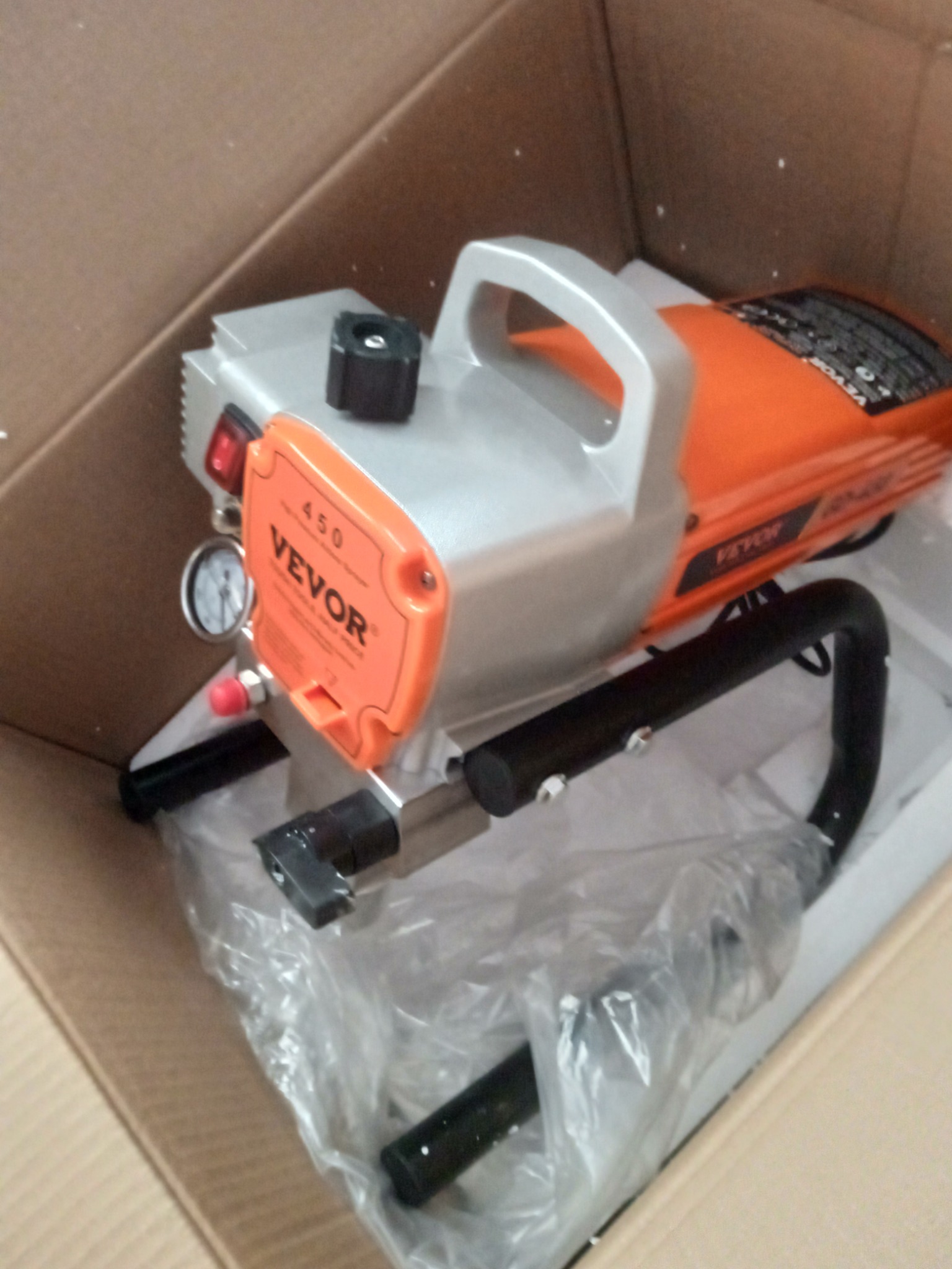 Sprzęt VEVOR 450 do malowania natryskowego, w kartonie. Srebrno-pomarańczowy korpus, czarne elementy. Widoczny manometr i włącznik.