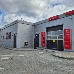 ROYAL CLEANING ARTUR RUSZKOWSKI - Nowoczesna, bezdotykowa myjnia samochodowa z szarym budynkiem i czerwonymi akcentami, widoczna z zewnątrz na tle pochmurnego nieba.