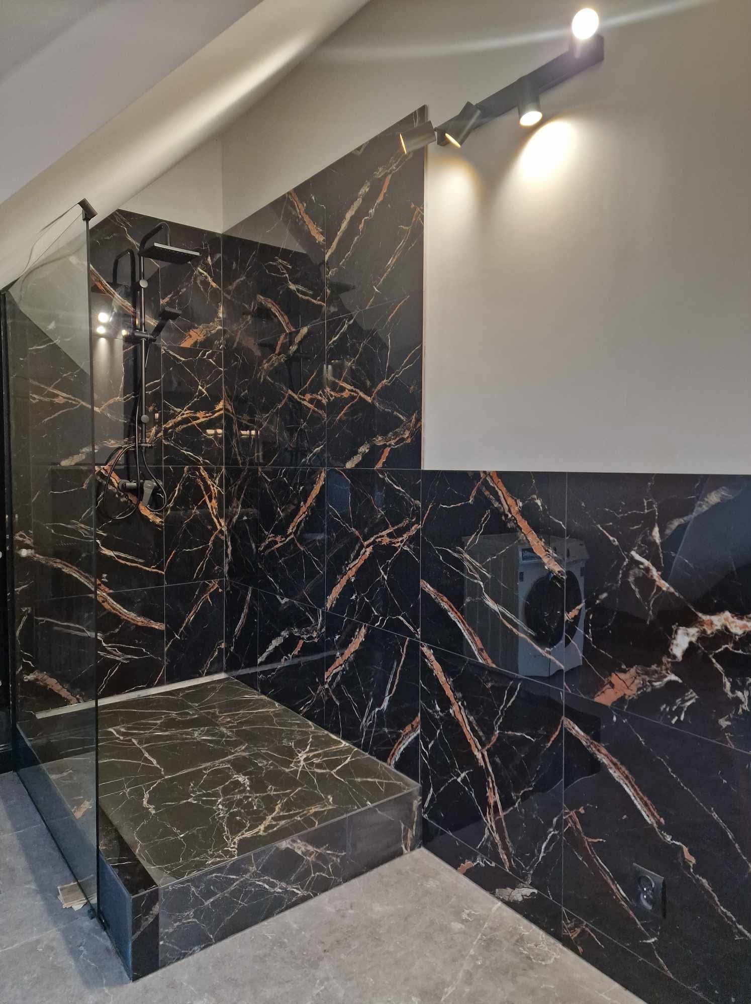 Luksusowa kabina prysznicowa z czarnymi płytkami marmurowymi i szklaną ścianką, oświetlona punktowo, w łazience na poddaszu.