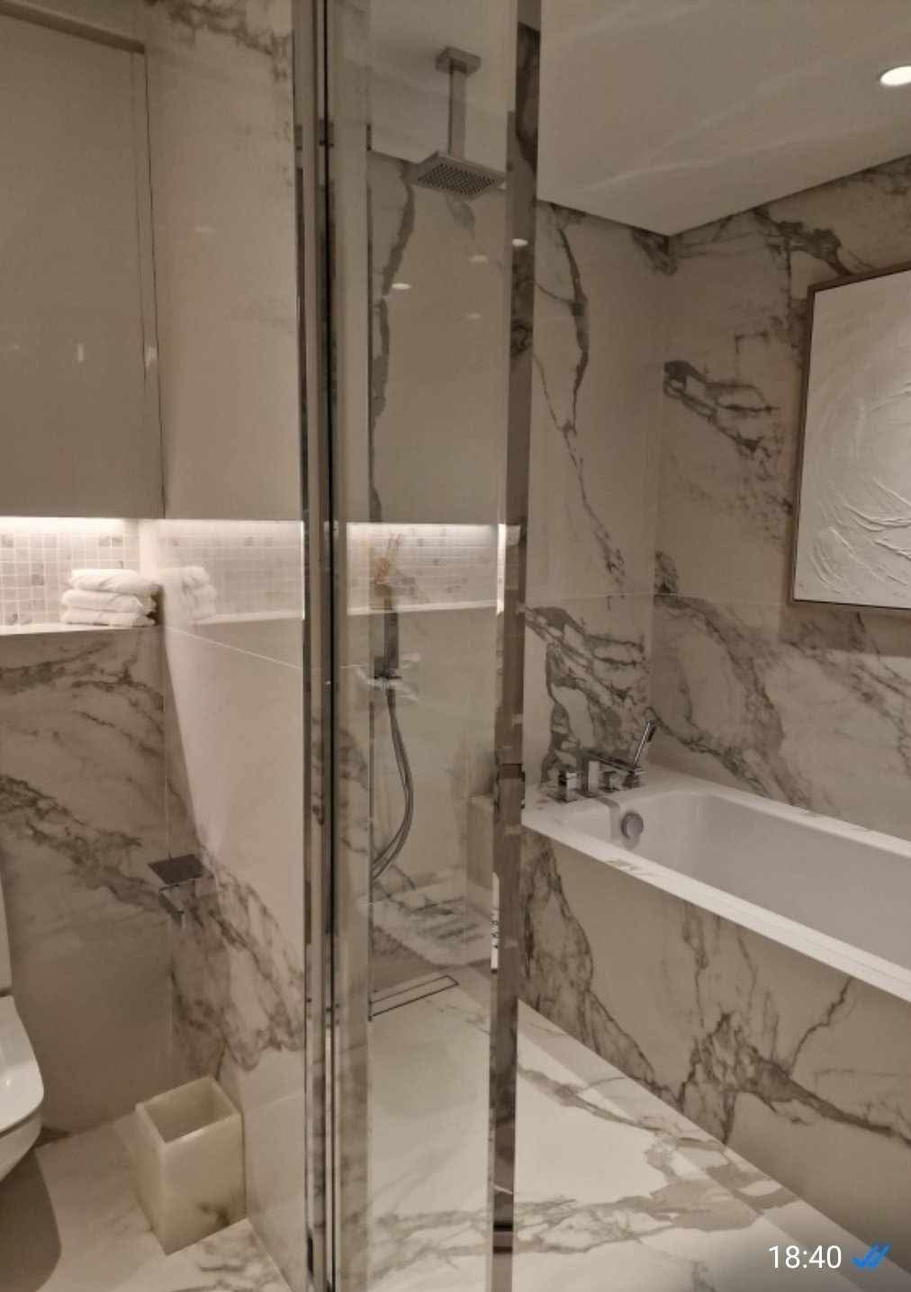Elegancka łazienka w bieli i marmurze z kabiną prysznicową typu walk-in, wanną i subtelnym oświetleniem punktowym, ukazująca nowoczesny design i wysoką jakość wykończenia.