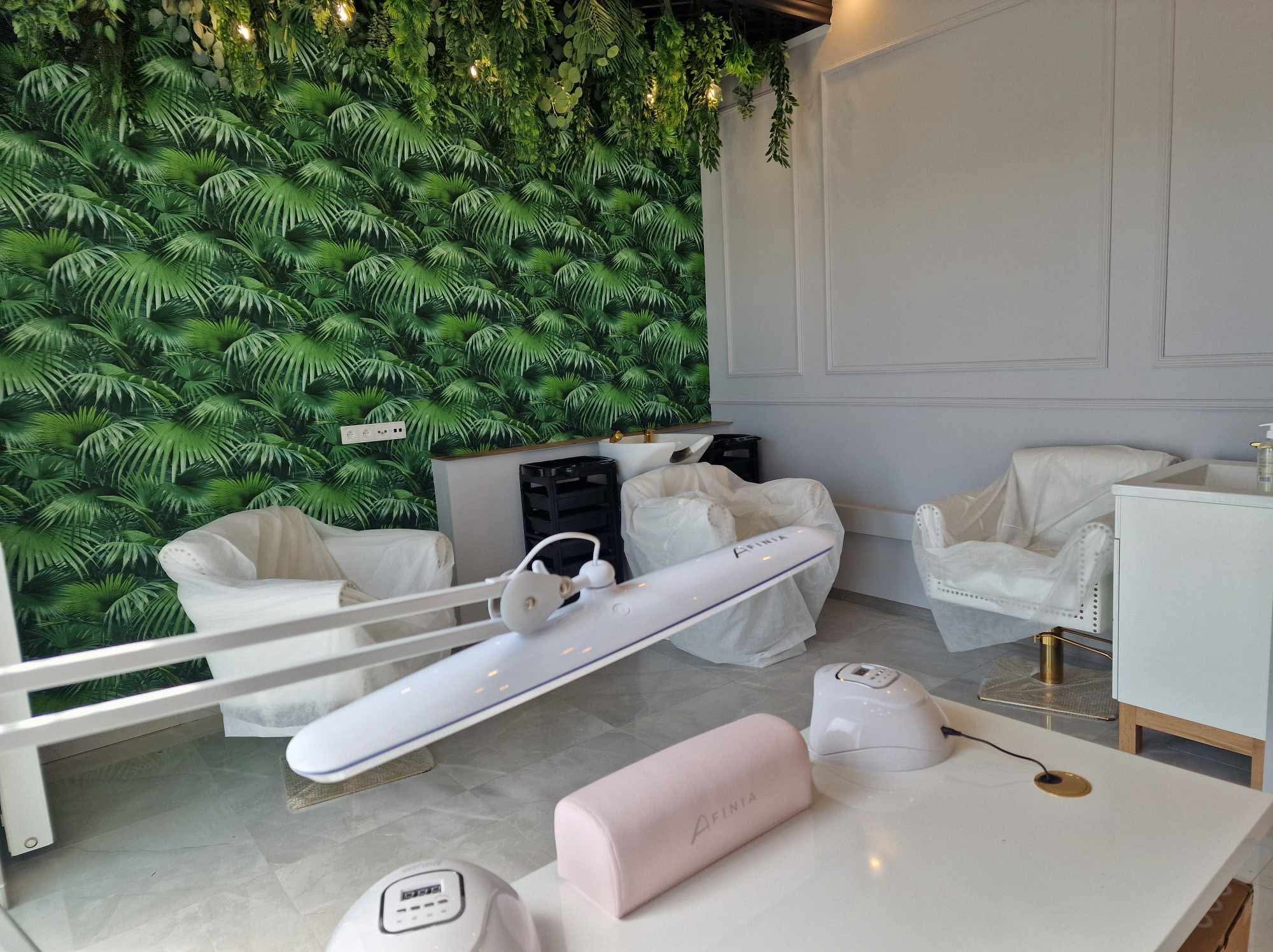 Salon kosmetyczny przed otwarciem: fotele zabezpieczone folią, ściana z motywem roślinnym, lampa do manicure i stół z wyposażeniem. Przygotowania do pracy.