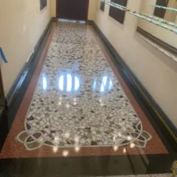 Błyszcząca, mozaikowa posadzka w korytarzu z wzorem dekoracyjnym. Widoczne odbicia światła i różnorodne kolory kamieni. Detal wykończenia podłogi w budynku.