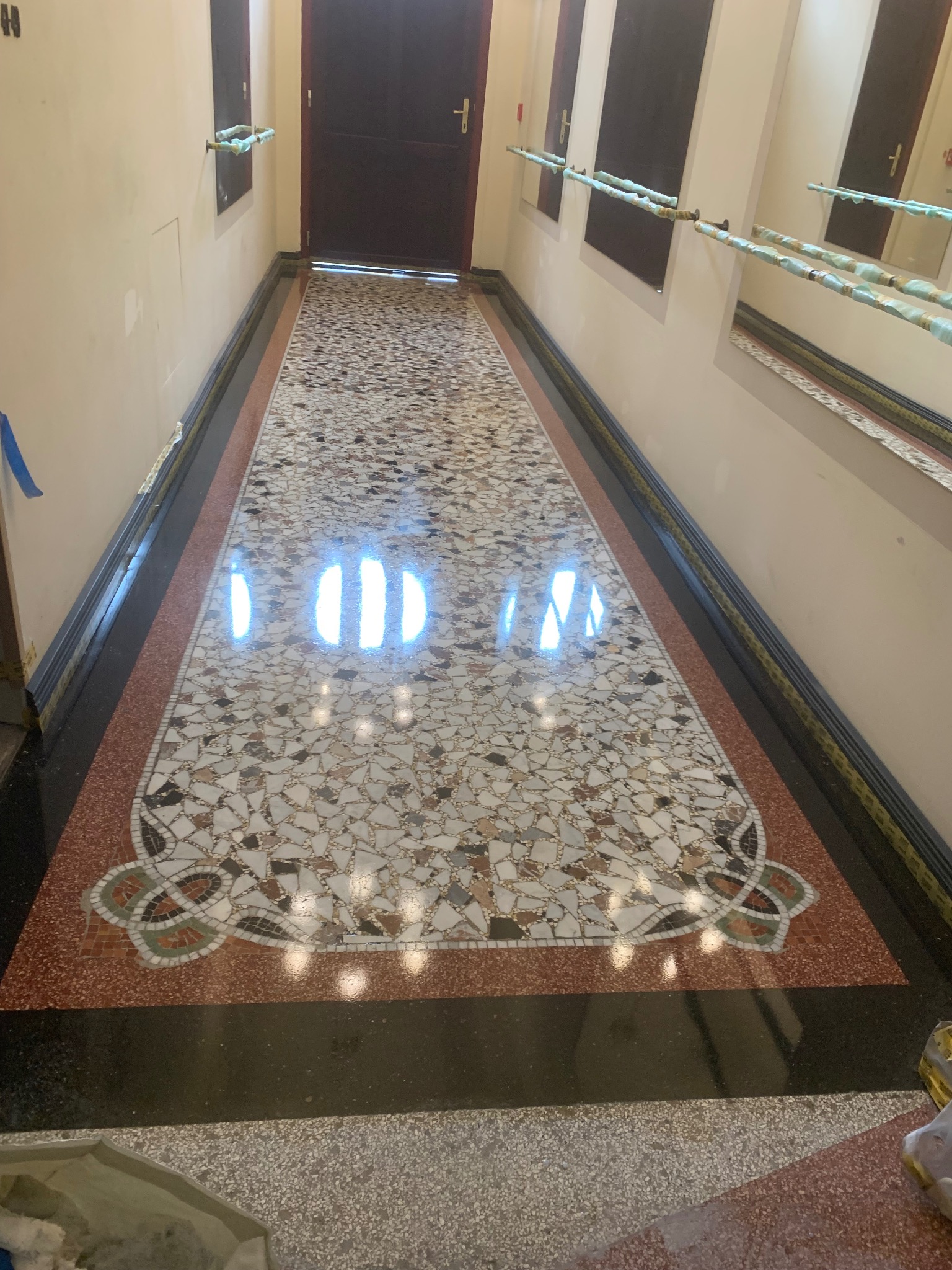 Błyszcząca, mozaikowa posadzka w korytarzu z wzorem dekoracyjnym. Widoczne odbicia światła i różnorodne kolory kamieni. Detal wykończenia podłogi w budynku.