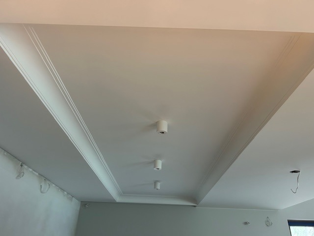 Biały sufit z dekoracyjnymi listwami i punktowym oświetleniem LED. Widok z dołu, podkreślający precyzję wykonania i nowoczesny design.