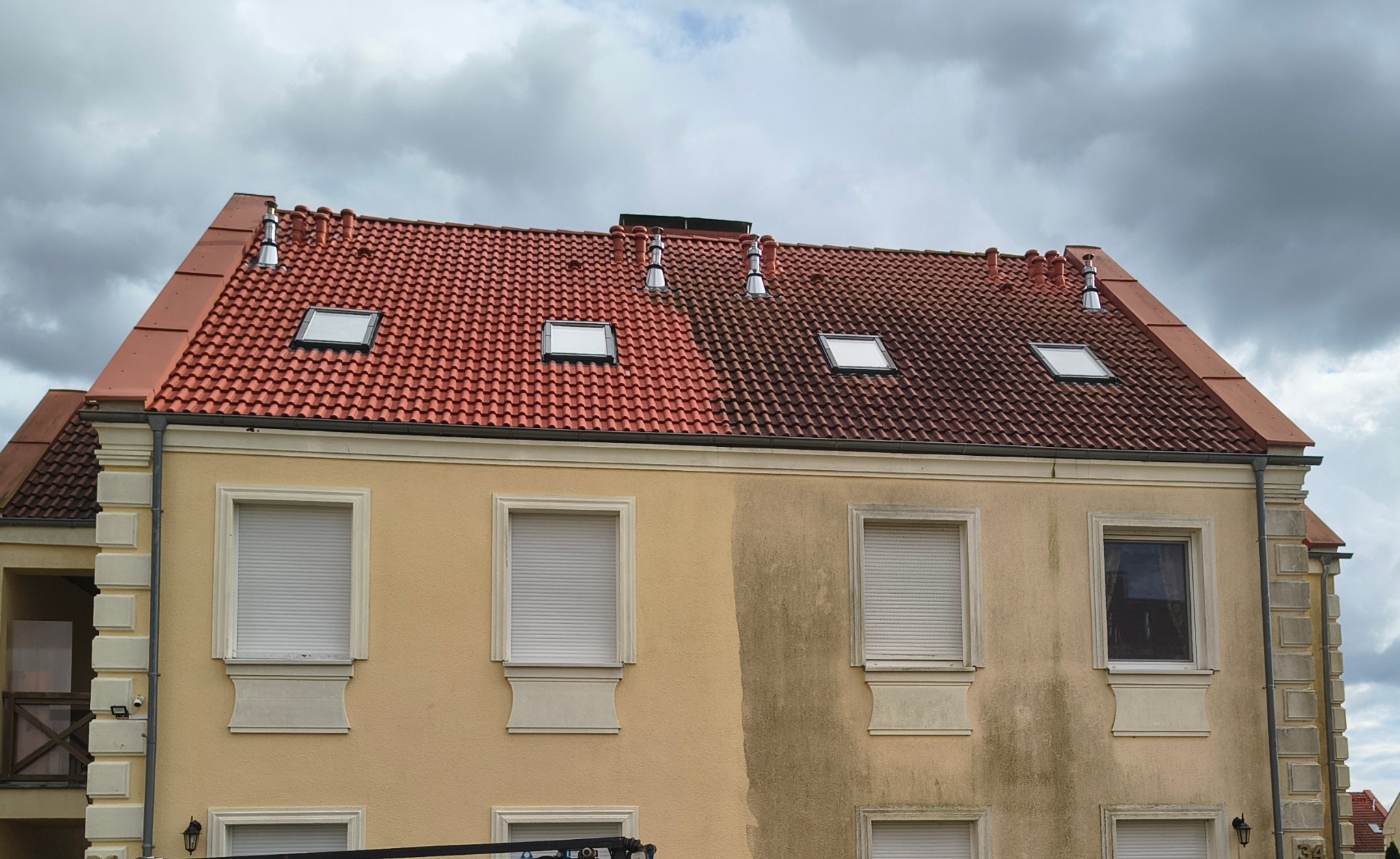 Budynek z częściowo umytą elewacją i dachem z czerwonej dachówki. Widoczna różnica w czystości między lewą a prawą stroną budynku.