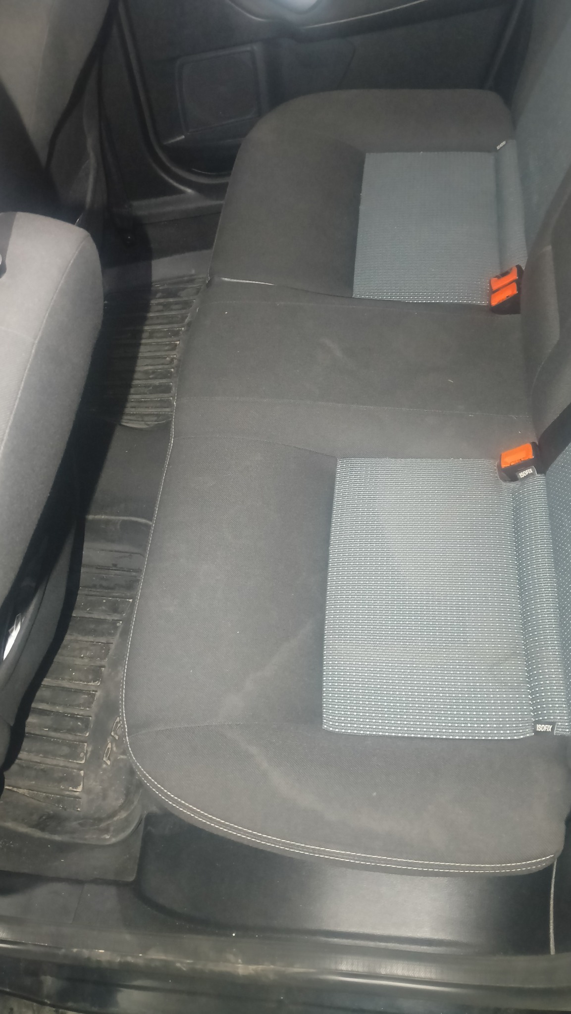 Tylna kanapa samochodu z widocznymi plamami i zabrudzeniami na ciemnej tapicerce. Widoczne mocowania ISOFIX i gumowe dywaniki w aucie.