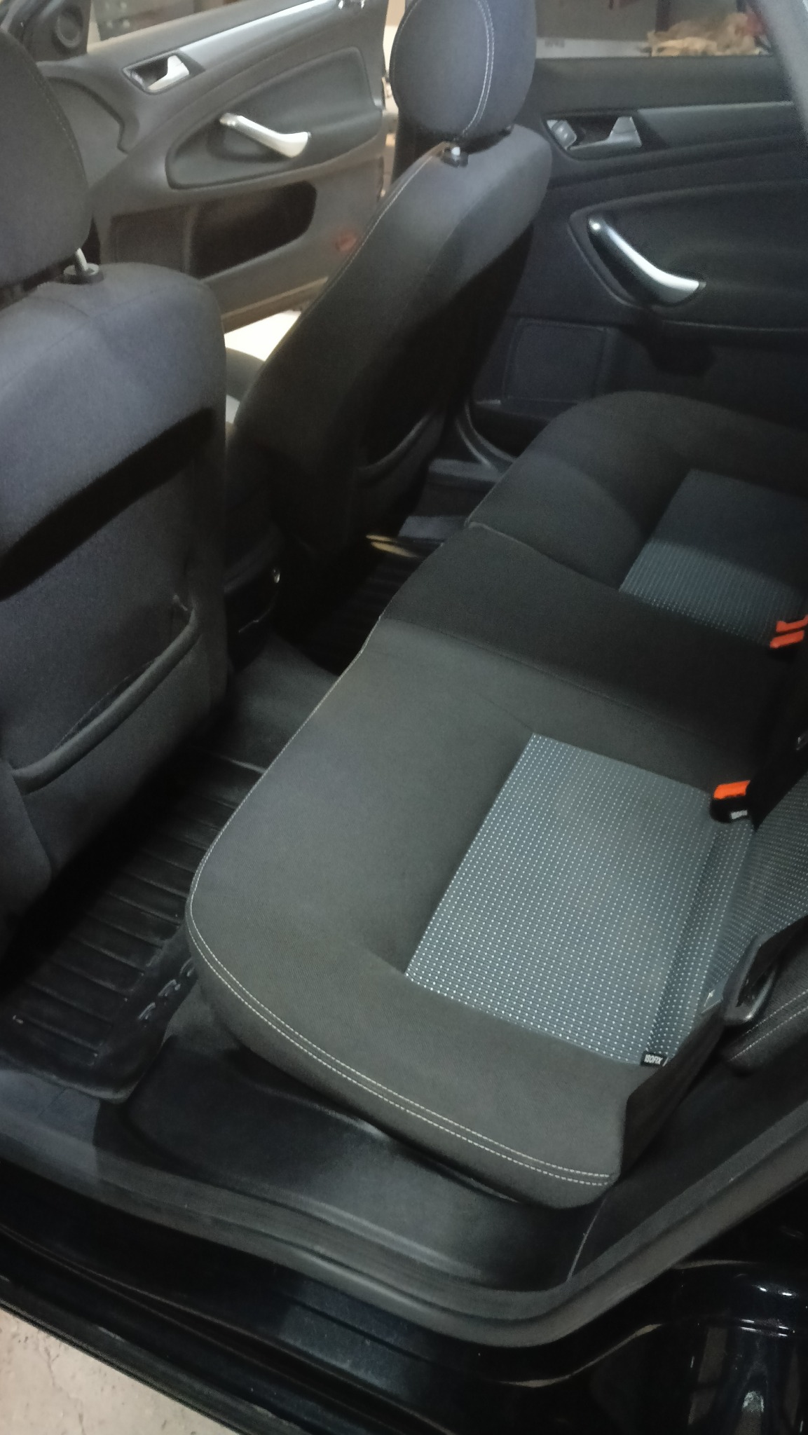 Wnętrze samochodu: tylne siedzenia z czarną tapicerką i szarym wzorem, widoczne zagłówki i fragmenty drzwi. Ciemna kolorystyka wnętrza.