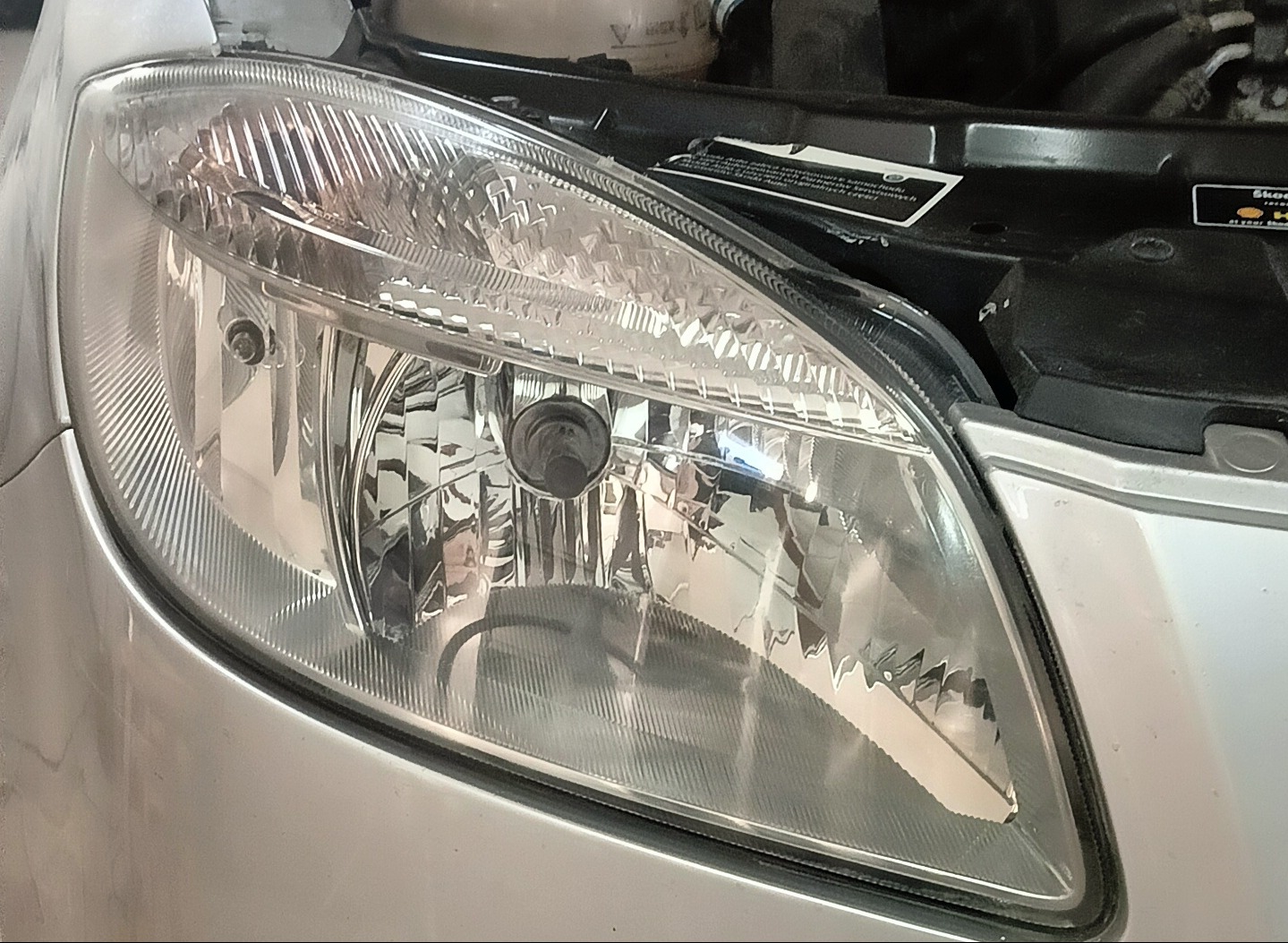 Reflektor samochodowy przed czyszczeniem w Pieńkach, widoczne zarysowania i zabrudzenia na szkle. Detailing reflektorów przywracający blask.