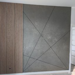 Witold Pawelec - Dekoracyjna ściana z drewnianymi lamelami po lewej i szarą fakturą z geometrycznym wzorem po prawej. Nowoczesny design wnętrza.