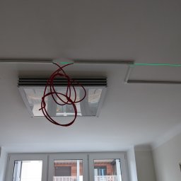 Z.U.O. SPÓŁKA Z OGRANICZONĄ ODPOWIEDZIALNOŚCIĄ - Montaż oświetlenia sufitowego: widoczne profile, lampy w kasetonach i przewody. Użycie lasera do wyznaczania linii. Etap prac instalacyjnych w jasnym wnętrzu.