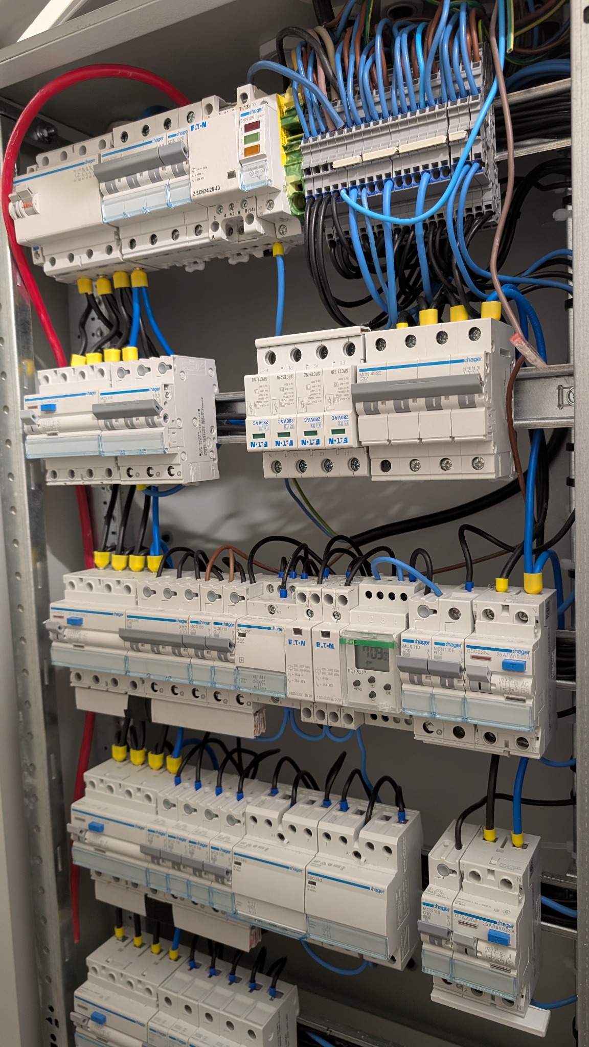 Rozdzielnia elektryczna z bezpiecznikami Hager i Eaton, okablowanie w kolorach niebieskim, czarnym i czerwonym, widok z bliska na zainstalowane komponenty.