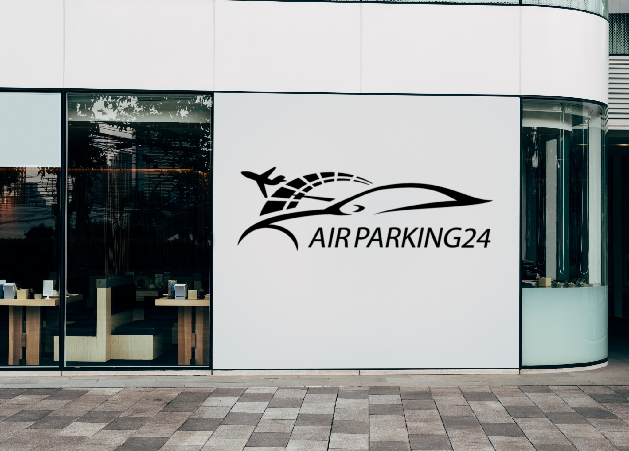 Logo 'AIR PARKING24' z motywem samolotu i samochodu umieszczone na białej ścianie budynku z przeszklonymi witrynami.