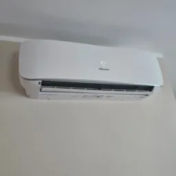 Biały klimatyzator Hisense z wyświetlaną temperaturą 21°C, zamontowany na jasnej ścianie w pomieszczeniu z żaluzjami w tle.