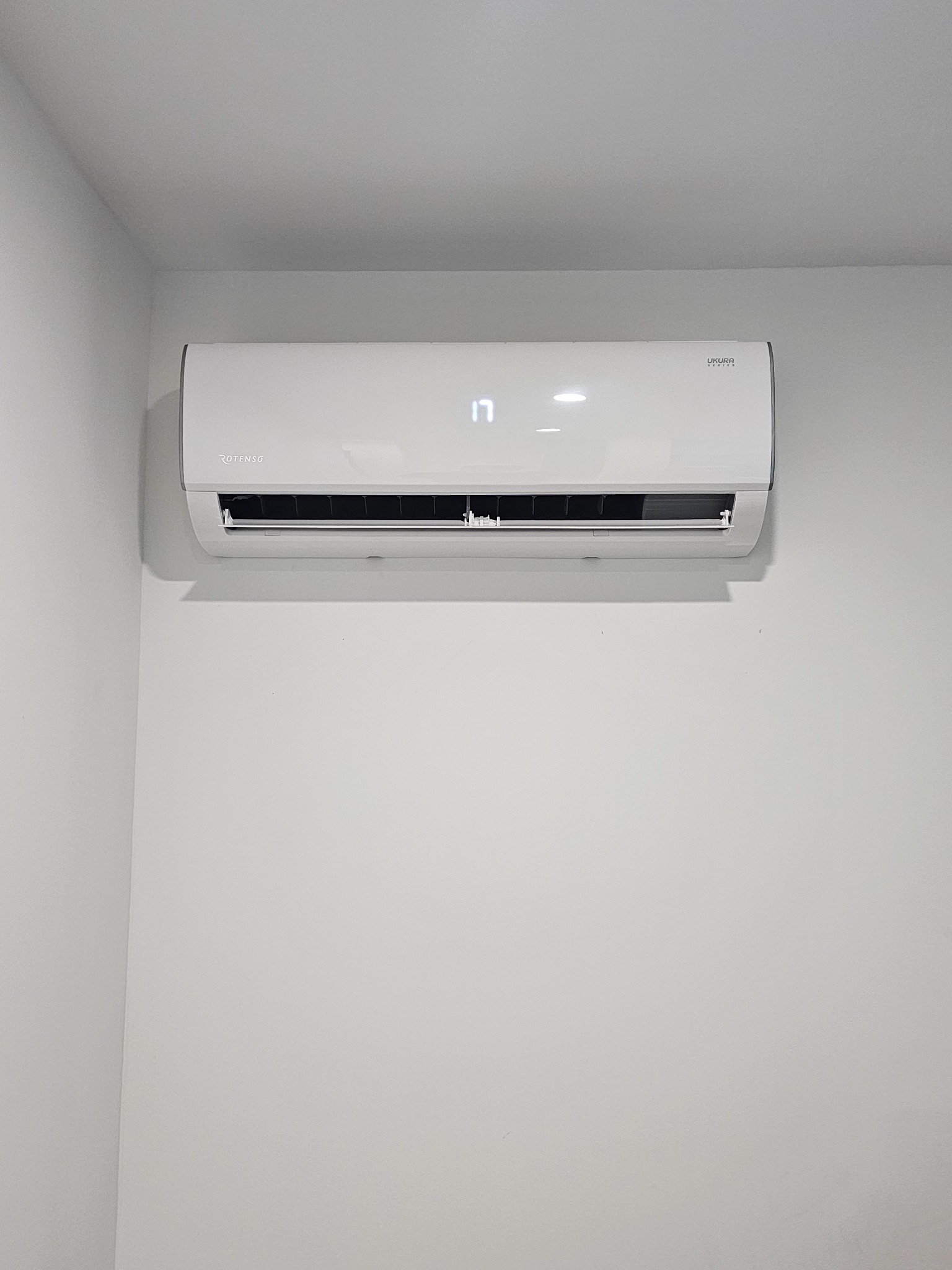 Biała klimatyzacja Rotenso Ukura, zamontowana na jasnej ścianie. Widoczny wyświetlacz z temperaturą 17 stopni. Minimalistyczny design.