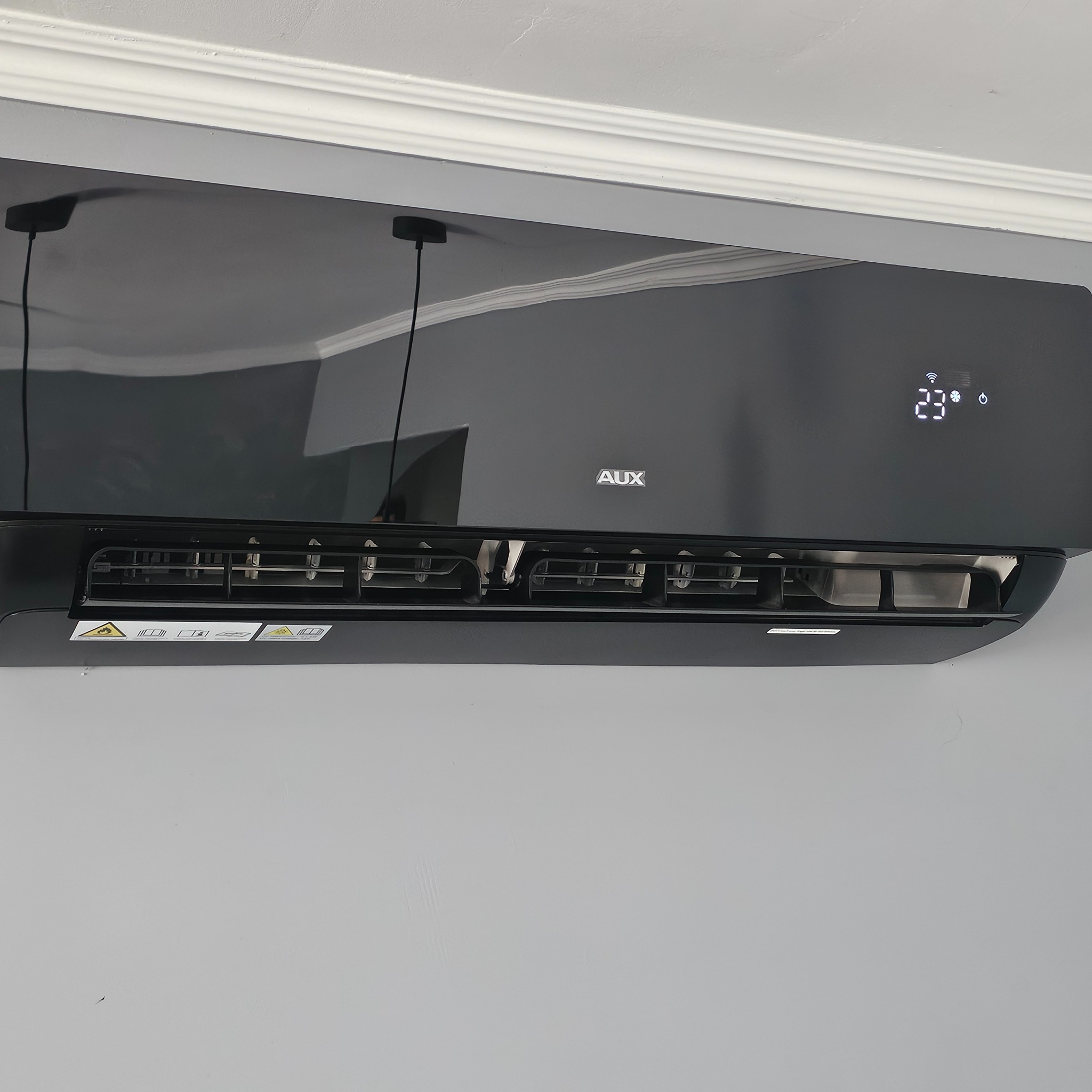 Czarny klimatyzator AUX zamontowany na ścianie w Siemieniu. Widoczny wyświetlacz z temperaturą 23 stopnie Celsjusza i żaluzje nawiewu.