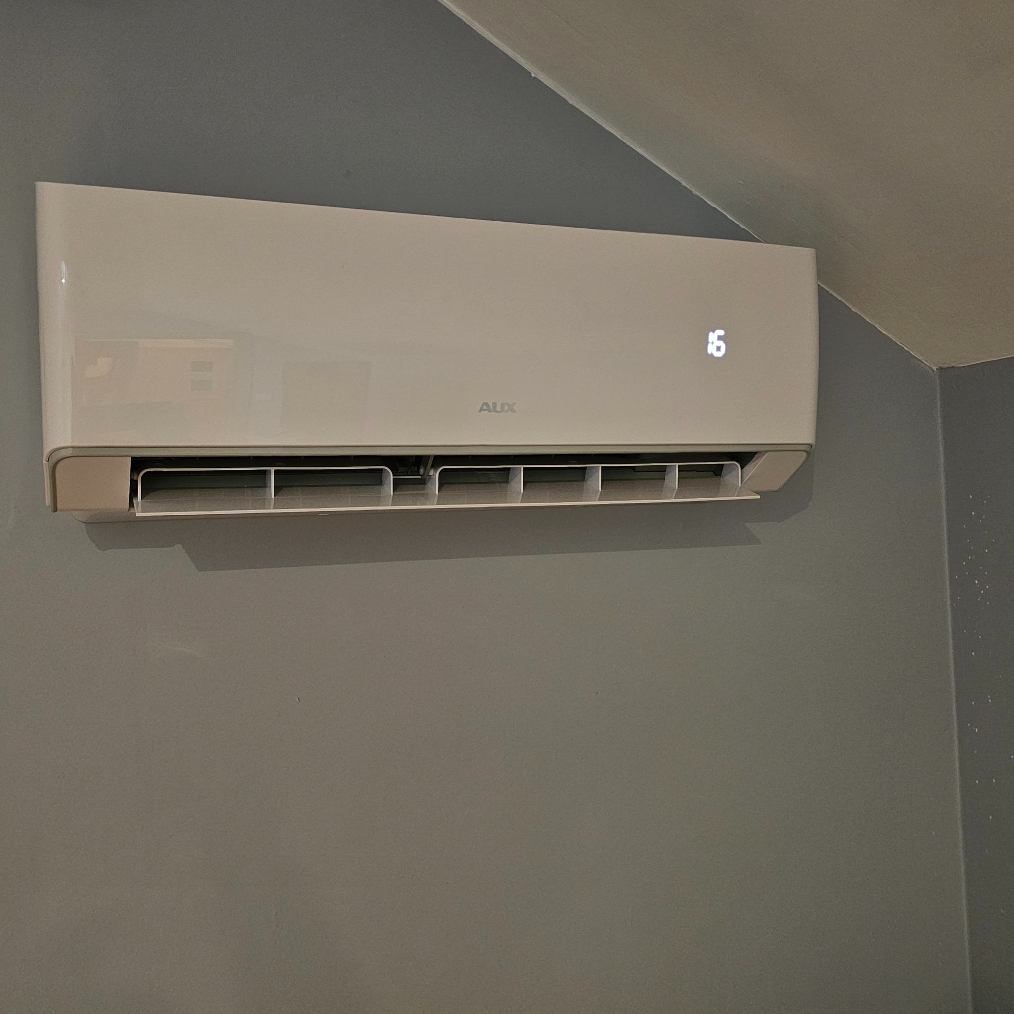 Biała klimatyzacja AUX na szarej ścianie. Widoczny wyświetlacz z temperaturą 16 stopni. Minimalistyczny design, nowoczesne wnętrze.