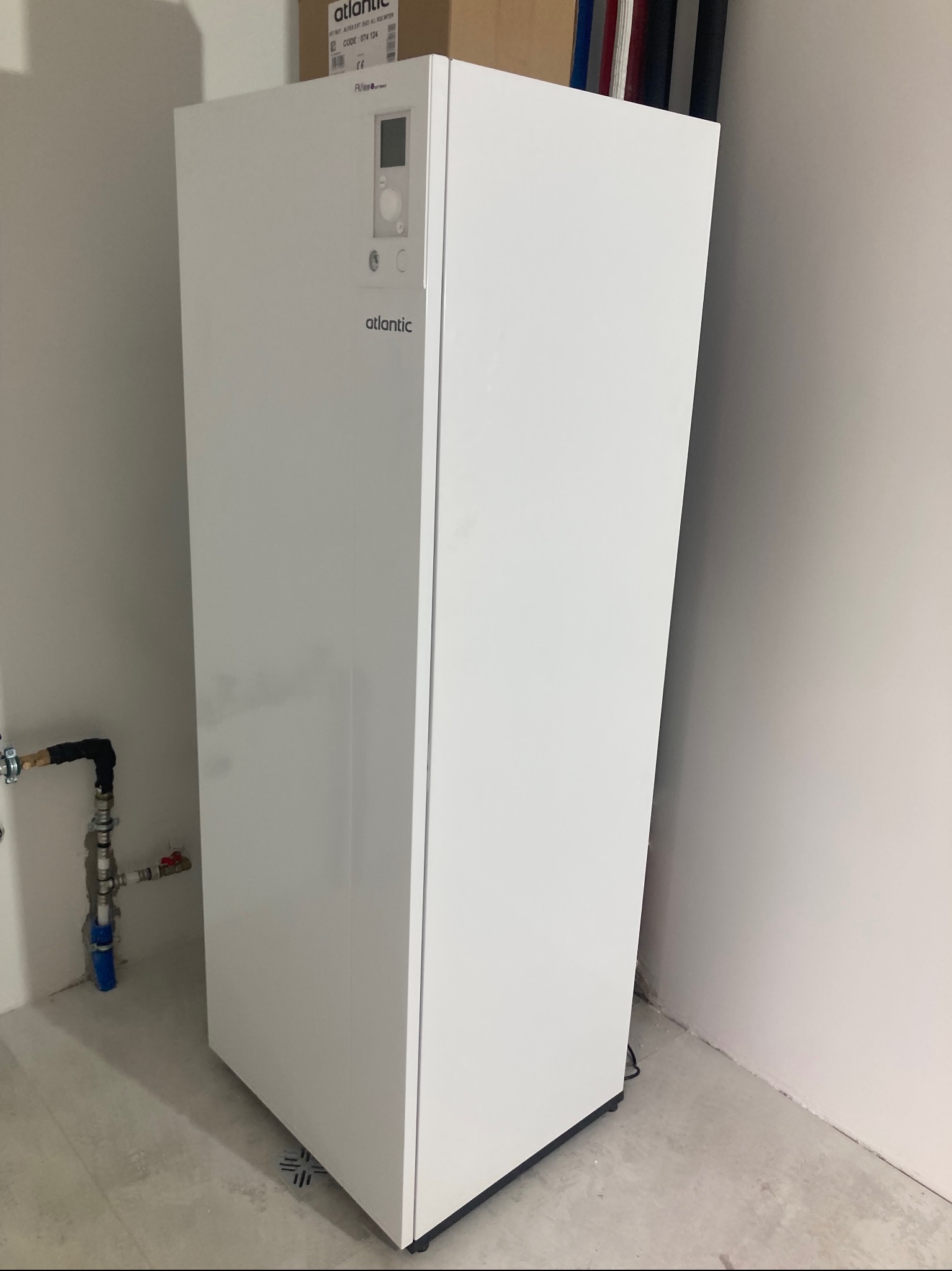 Biały, nowoczesny piec gazowy Atlantic, zainstalowany w pomieszczeniu z surowym betonem na podłodze i widocznymi rurami. Minimalistyczny design, czyste linie.