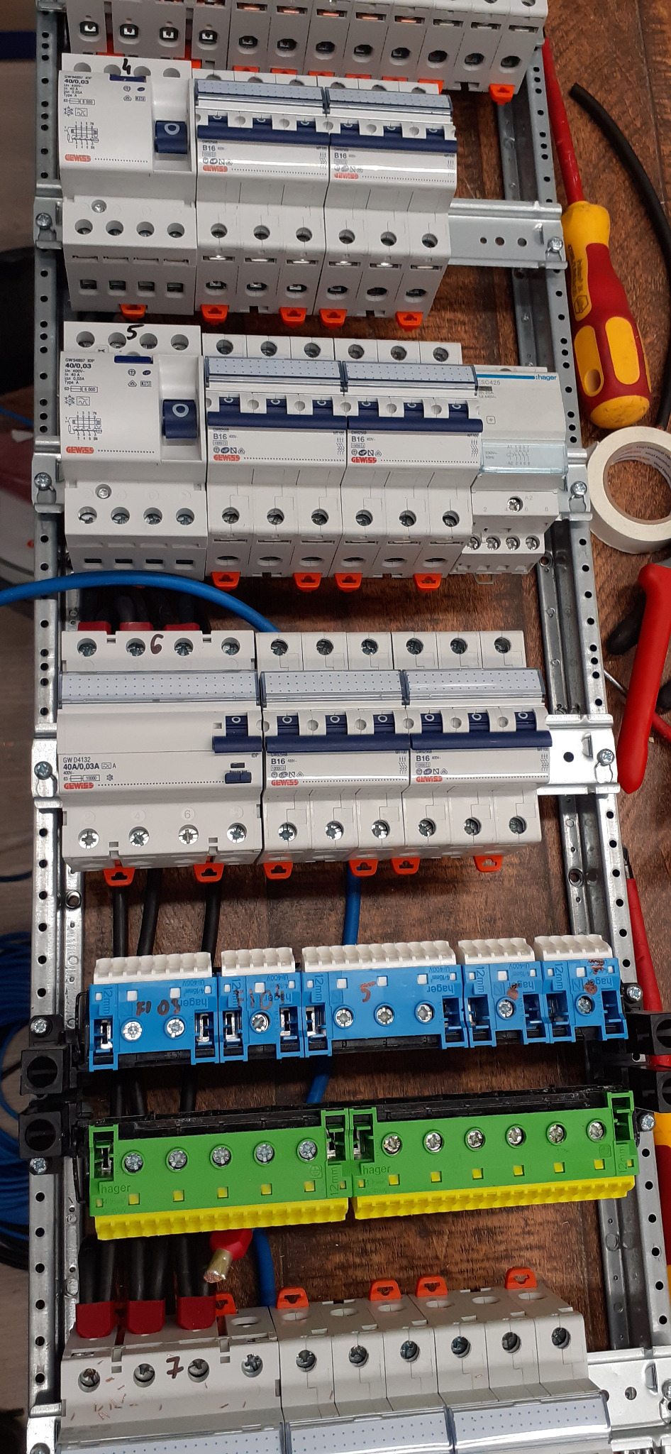 Rozdzielnia elektryczna z zamontowanymi bezpiecznikami i przewodami, widok z góry. Widoczne narzędzia monterskie, listwy zaciskowe i elementy instalacji elektrycznej.