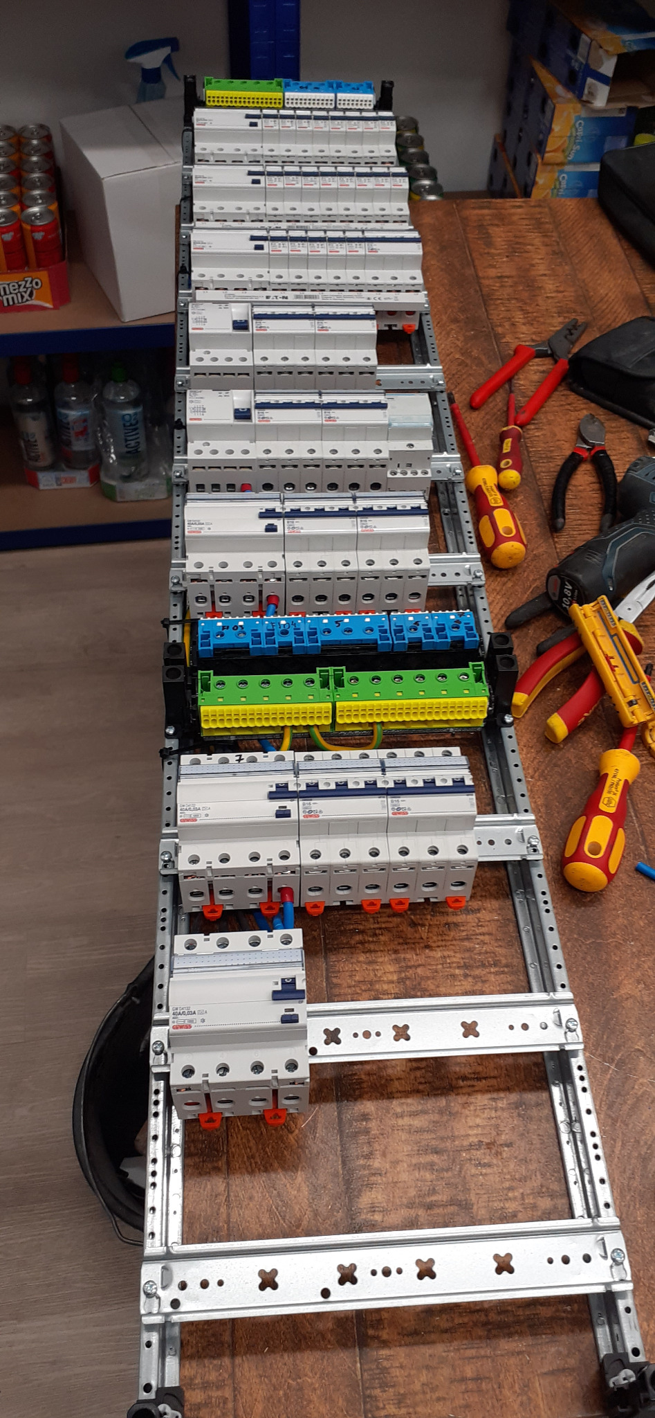 Rozdzielnica elektryczna z zamontowanymi zabezpieczeniami, widoczne narzędzia na drewnianym blacie, ułożone pionowo.