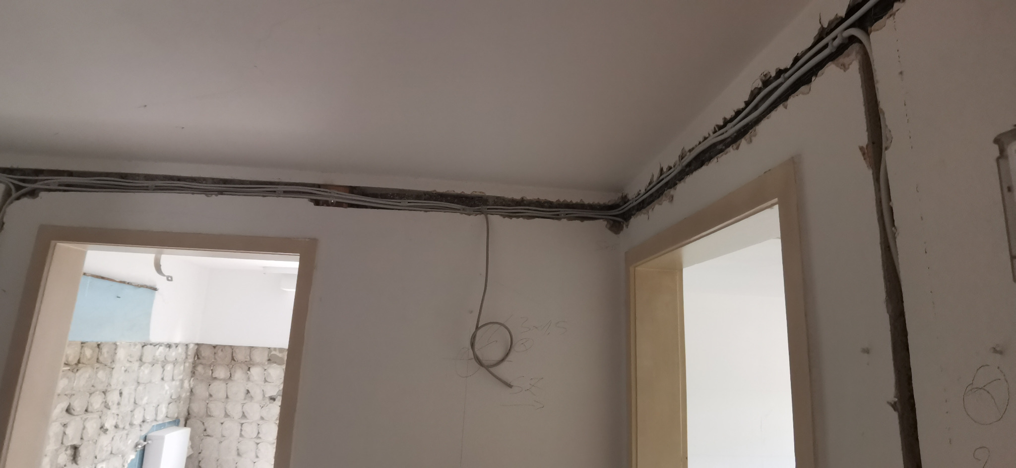 Instalacja elektryczna w bruzdach pod sufitem, kable prowadzone wzdłuż ścian. Widoczne ślady po kuciu i przygotowaniu podłoża.