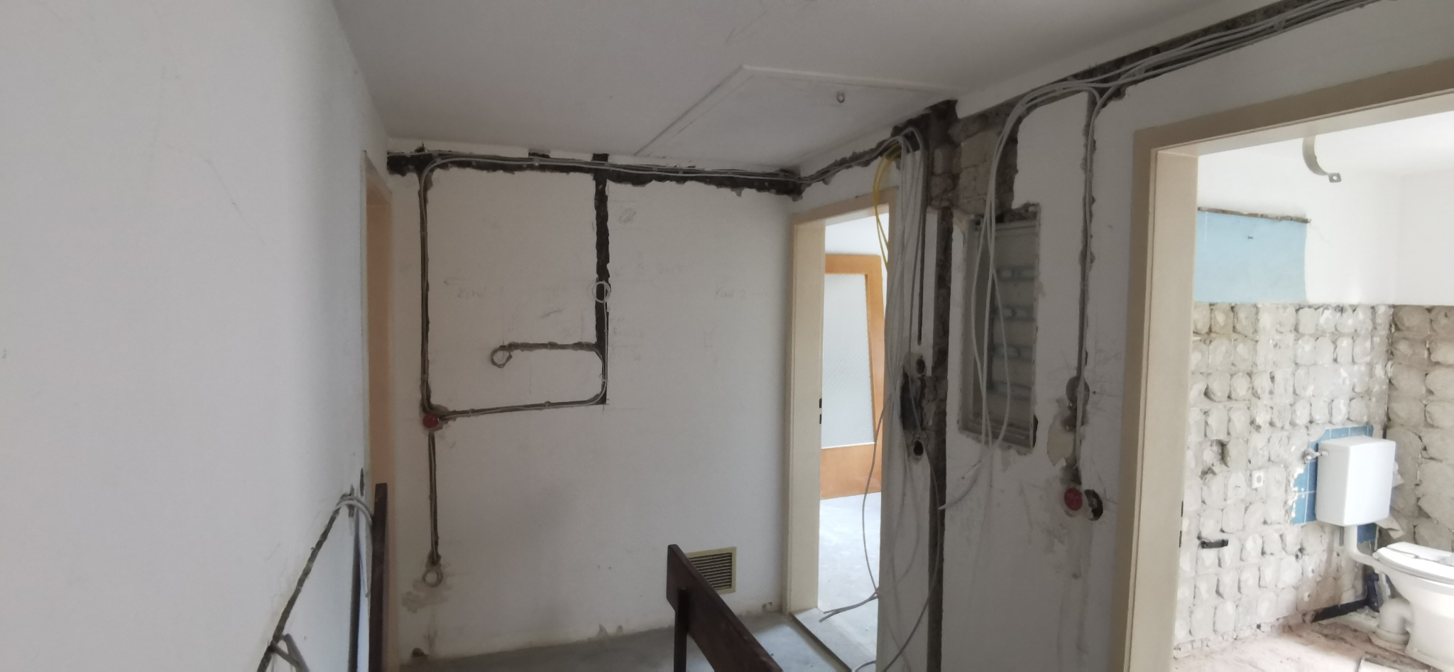 Przygotowanie pod instalację elektryczną w remontowanym wnętrzu: wyżłobione bruzdy w ścianach, kable ułożone w korytach, widoczne puszki instalacyjne. W tle wyremontowana łazienka.