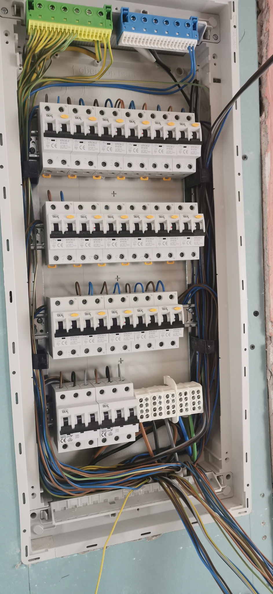 Rozdzielnica elektryczna z zamontowanymi bezpiecznikami i podłączonymi przewodami w różnych kolorach, widok z góry, detale połączeń.