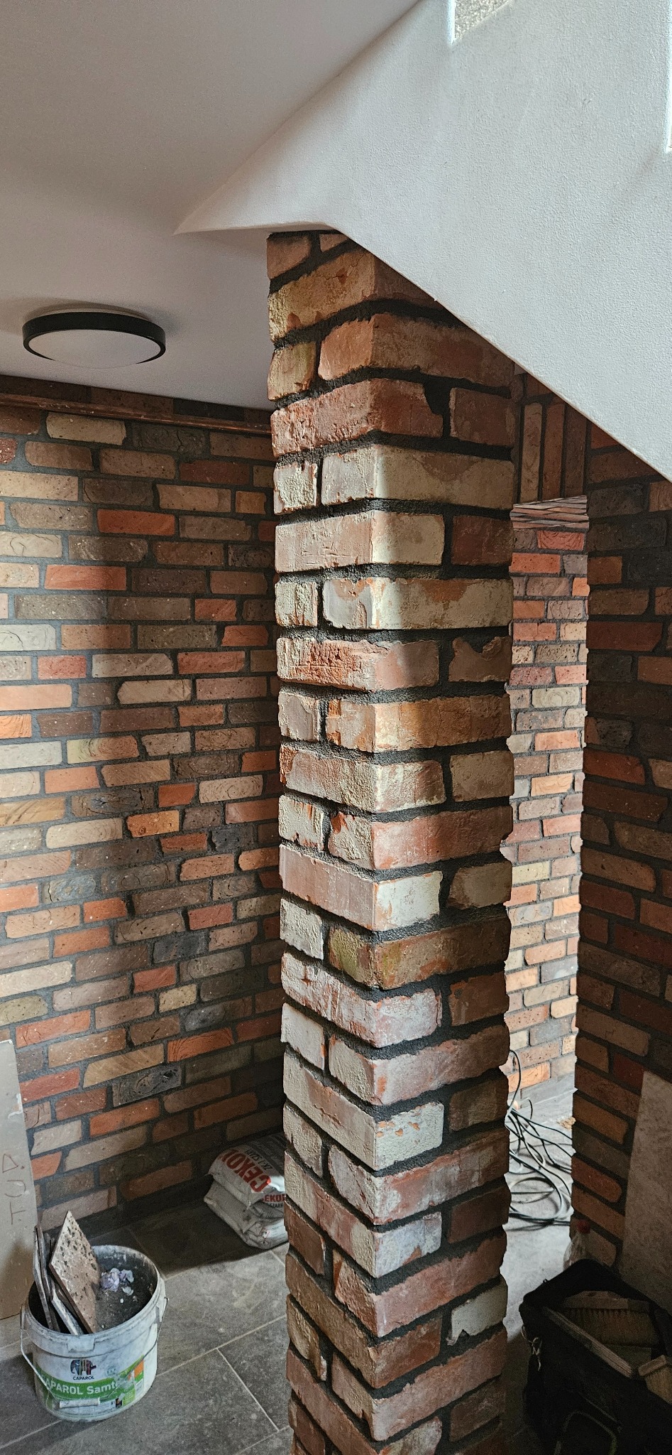 Wnętrze z dekoracyjną ścianą z cegły i filarem z cegły klinkierowej, widoczne narzędzia i materiały budowlane. Element wykończenia wnętrza.