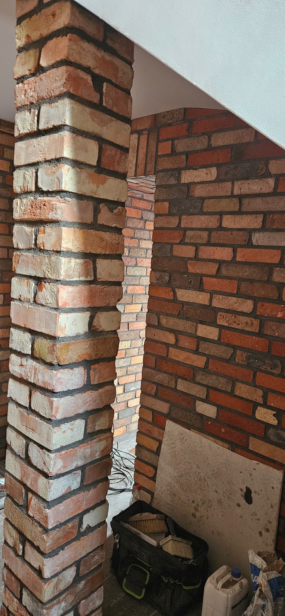 Wykończona ściana z cegły klinkierowej i filar w Krotoszynie. Widoczna torba z narzędziami murarskim. Dekoracyjne wykończenie wnętrza.