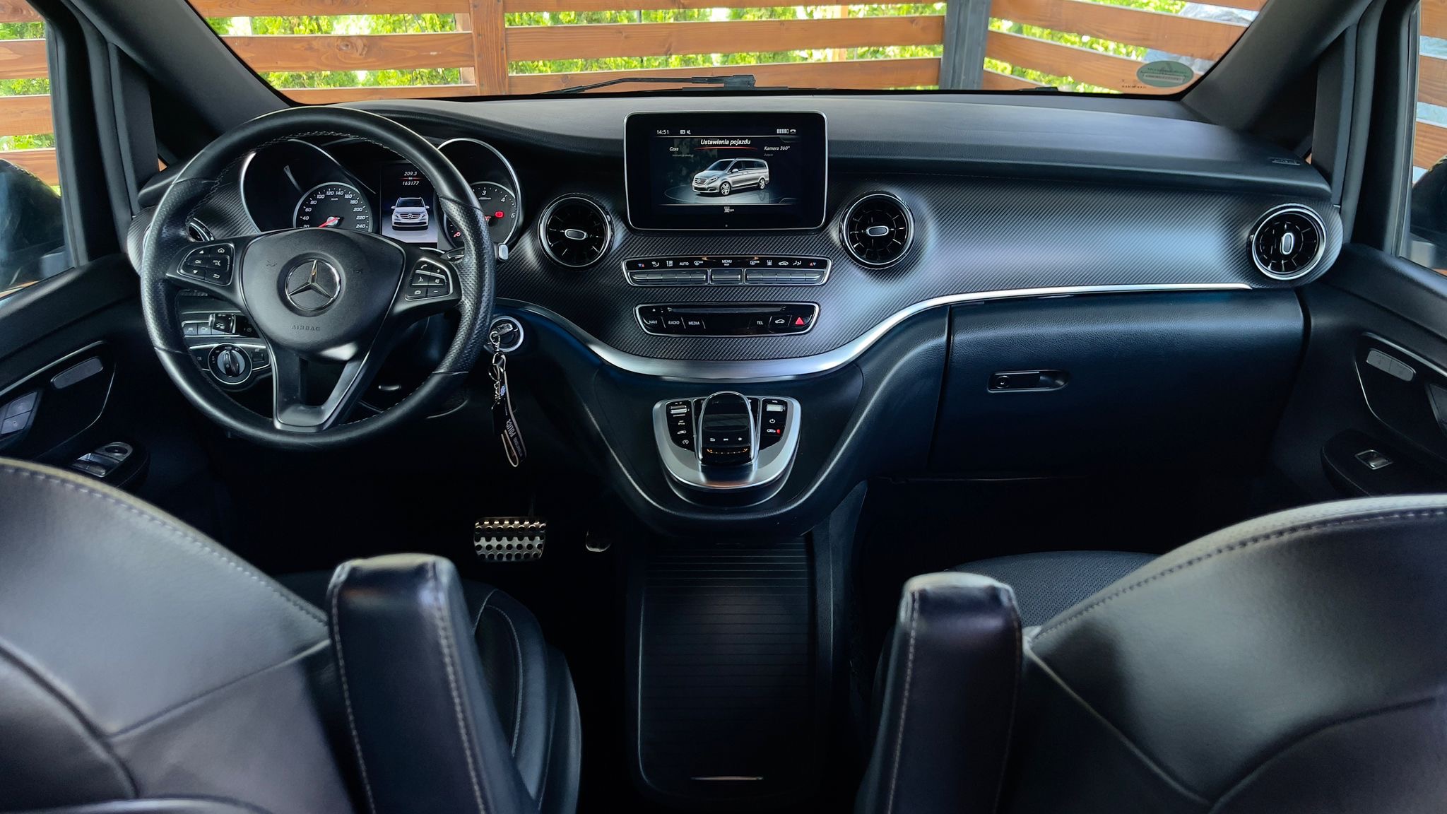 Wnętrze luksusowego samochodu Mercedes V-klasy z elegancką deską rozdzielczą, skórzanymi fotelami i elementami wykończenia z włókna węglowego. Widok z tylnych siedzeń.