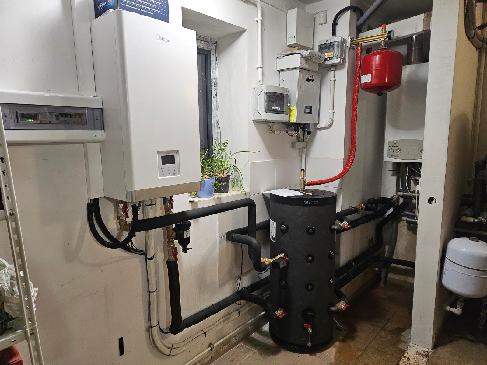 Nowoczesny piec gazowy Midea, zbiornik akumulacyjny Aquatec i instalacja CO w kotłowni z oknem, na tle białych ścian i płytek podłogowych.