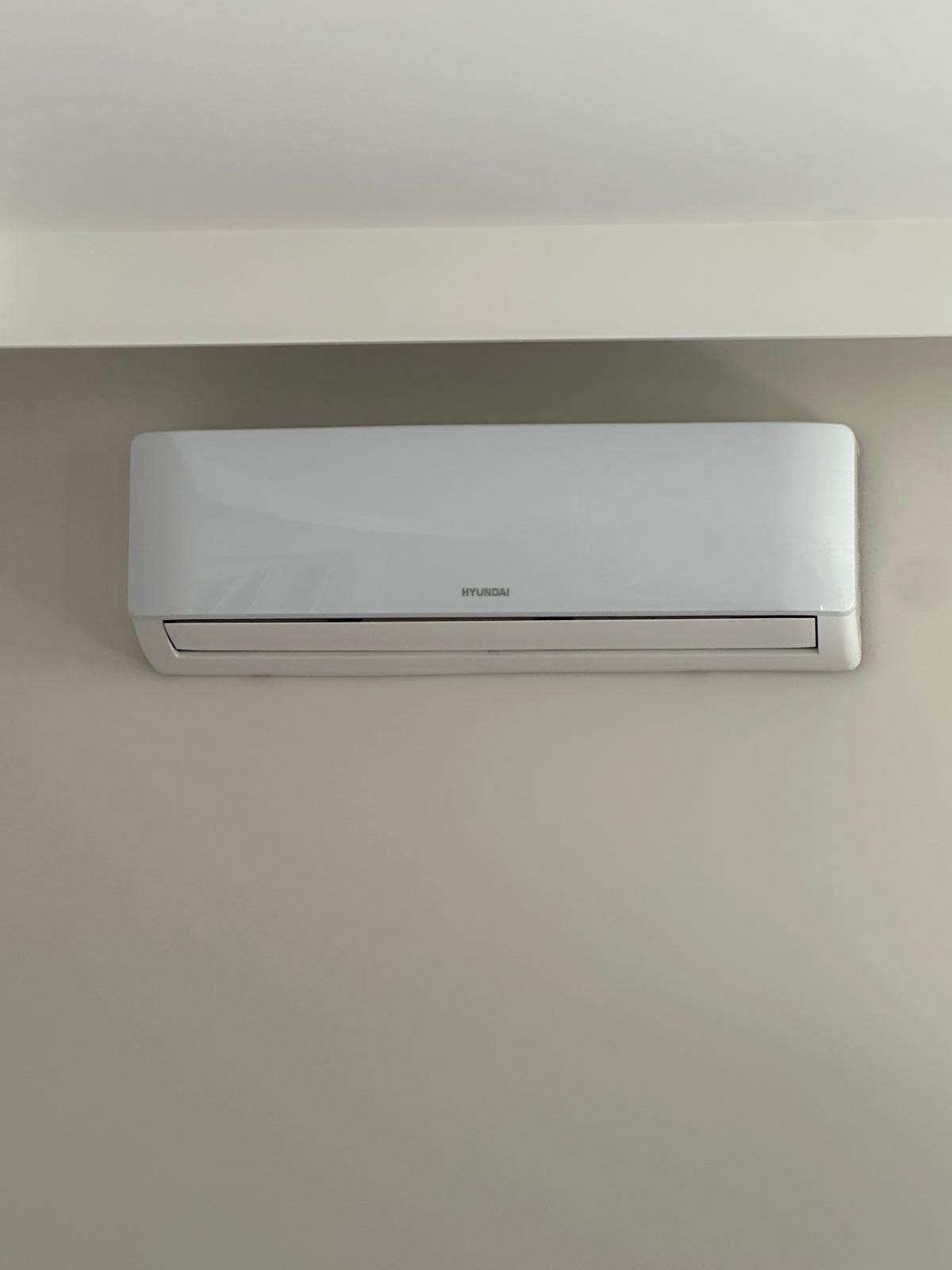 Biały klimatyzator Hyundai zamontowany na jasnej ścianie, widok z przodu. Widoczne proste linie urządzenia i minimalistyczny design. Nowoczesne rozwiązanie chłodnicze w pomieszczeniu.