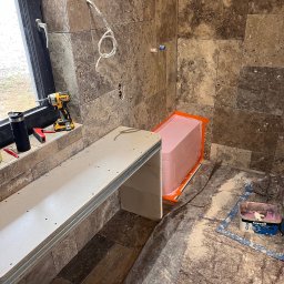 Józef Zubek Z BUD - Remont łazienki w trakcie: obudowa wanny z różowego styropianu, płytki trawertyn, narzędzia DeWalt na parapecie, płyta GK na stelażu.