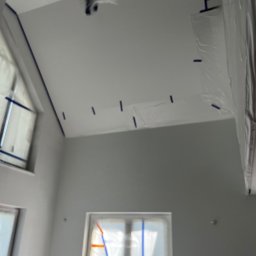 Józef Zubek Z BUD - Przygotowane do malowania wnętrze z oknami zabezpieczonymi folią i taśmą malarską, sufit i ściany po gruntowaniu. Widok z dołu.