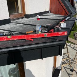 Józef Zubek Z BUD - Balkon po remoncie z czarną zabudową, narzędzia pracy na powierzchni. Widoczna drabina i fragment elewacji budynku.