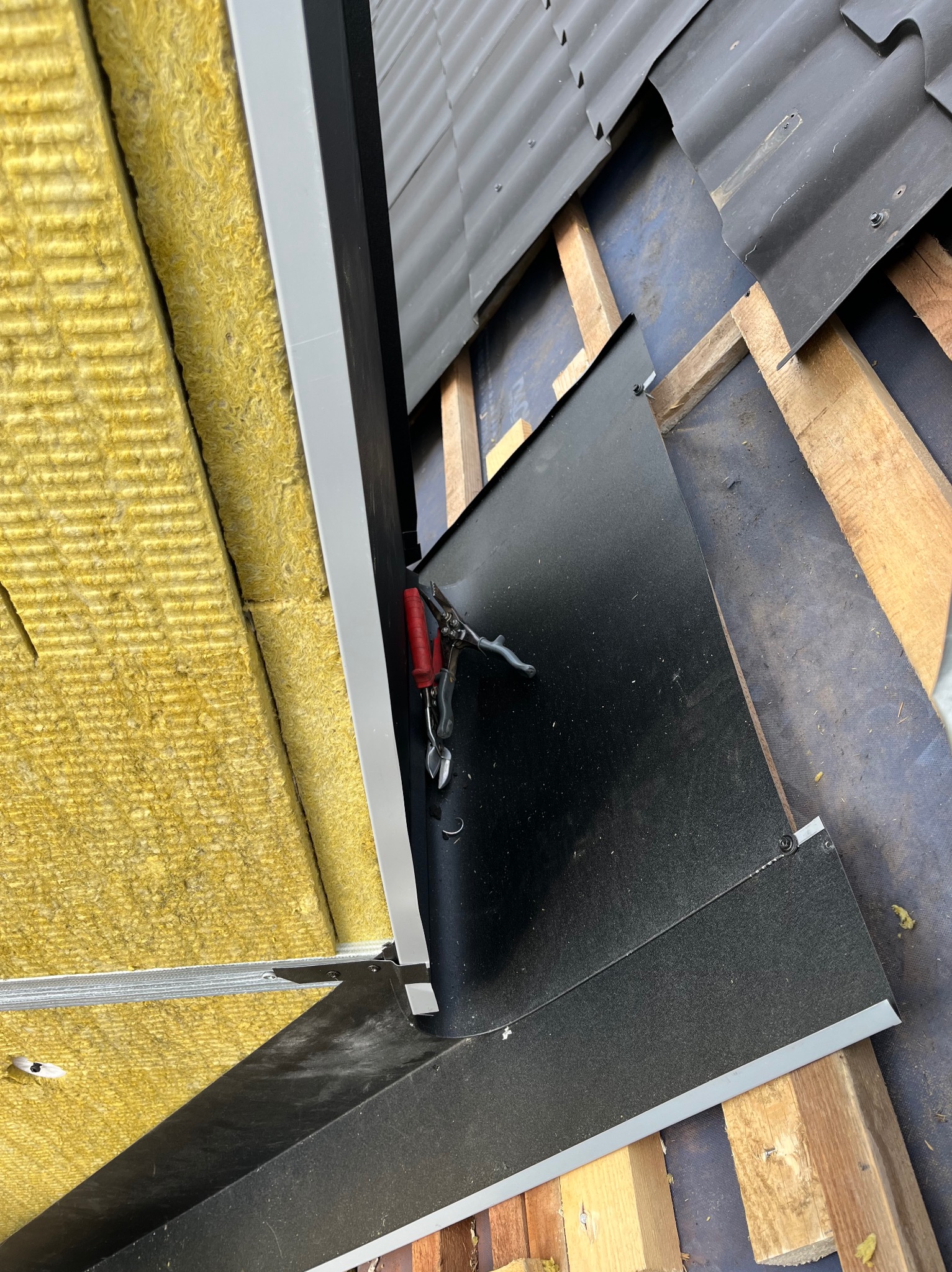 Ocieplenie balkonu wełną mineralną, widoczne narzędzia dekarskie i fragment konstrukcji z czarnej blachy. Ujęcie z góry, ostre światło.